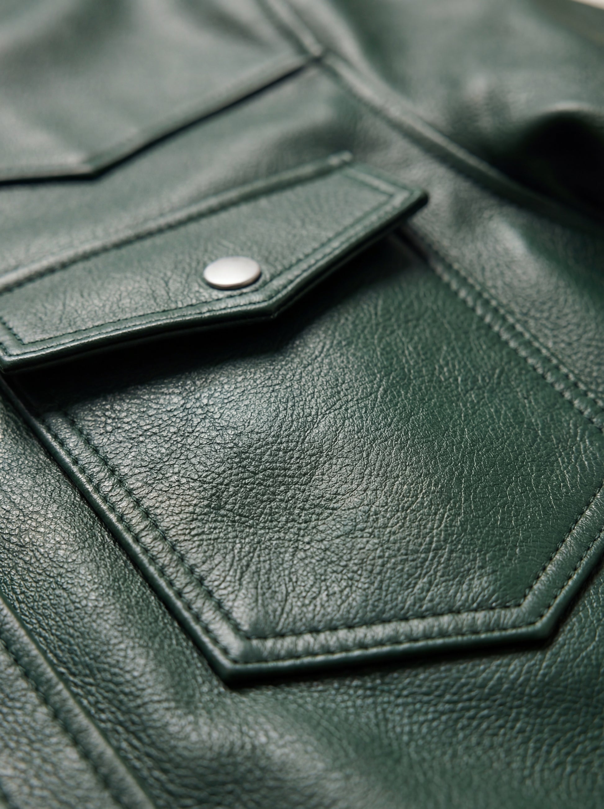 Macro shot of grained green leather texture and silver snap button detail on western shirt. The Cillian by Maverick Jacket.