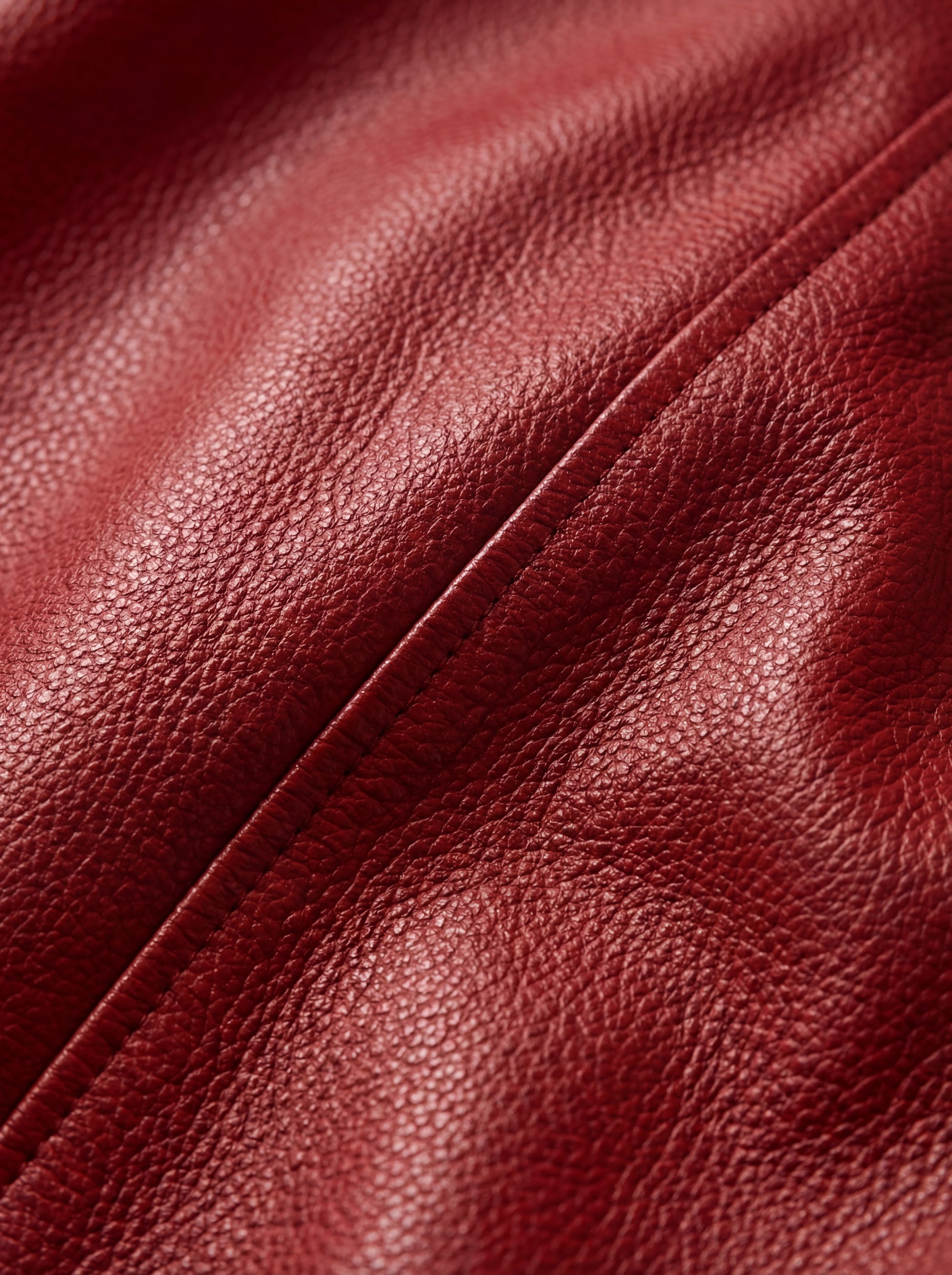 Macro shot of grained red leather texture and tonal stitching detail on bomber jacket. The Isla by Maverick Jacket.