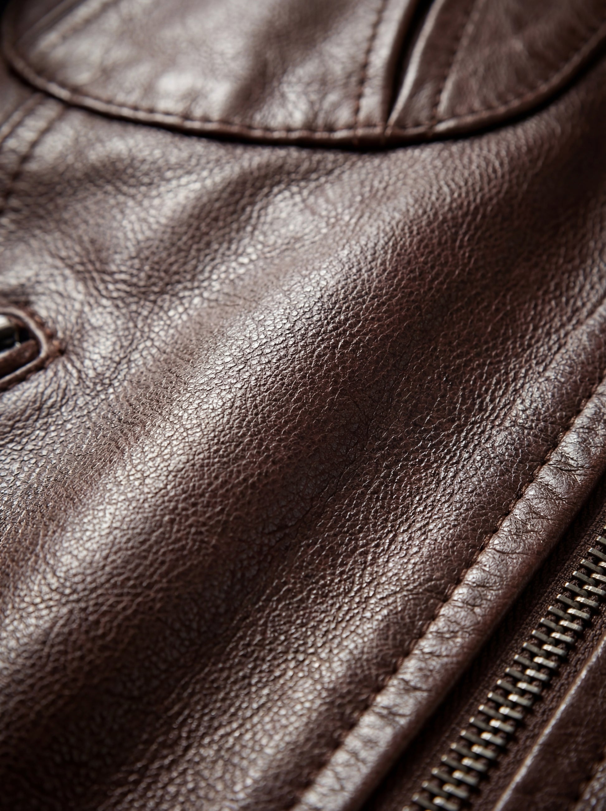 Macro shot of pebbled brown leather texture and metal zipper track on bomber jacket. The Sienna by Maverick Jacket.