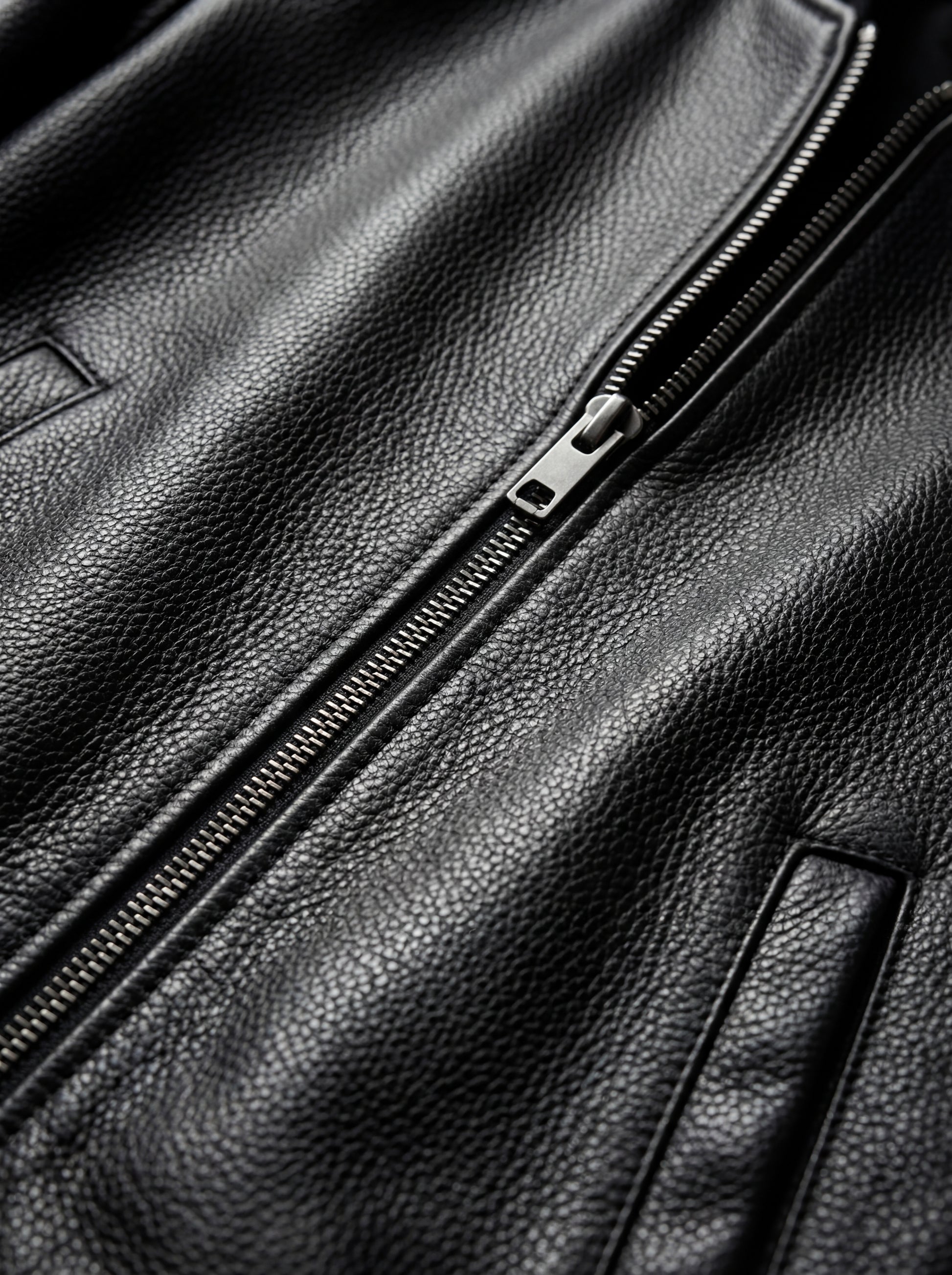 Macro shot of pebbled black leather texture and silver metal zipper puller on bomber jacket. The Roxy by Maverick Jacket.