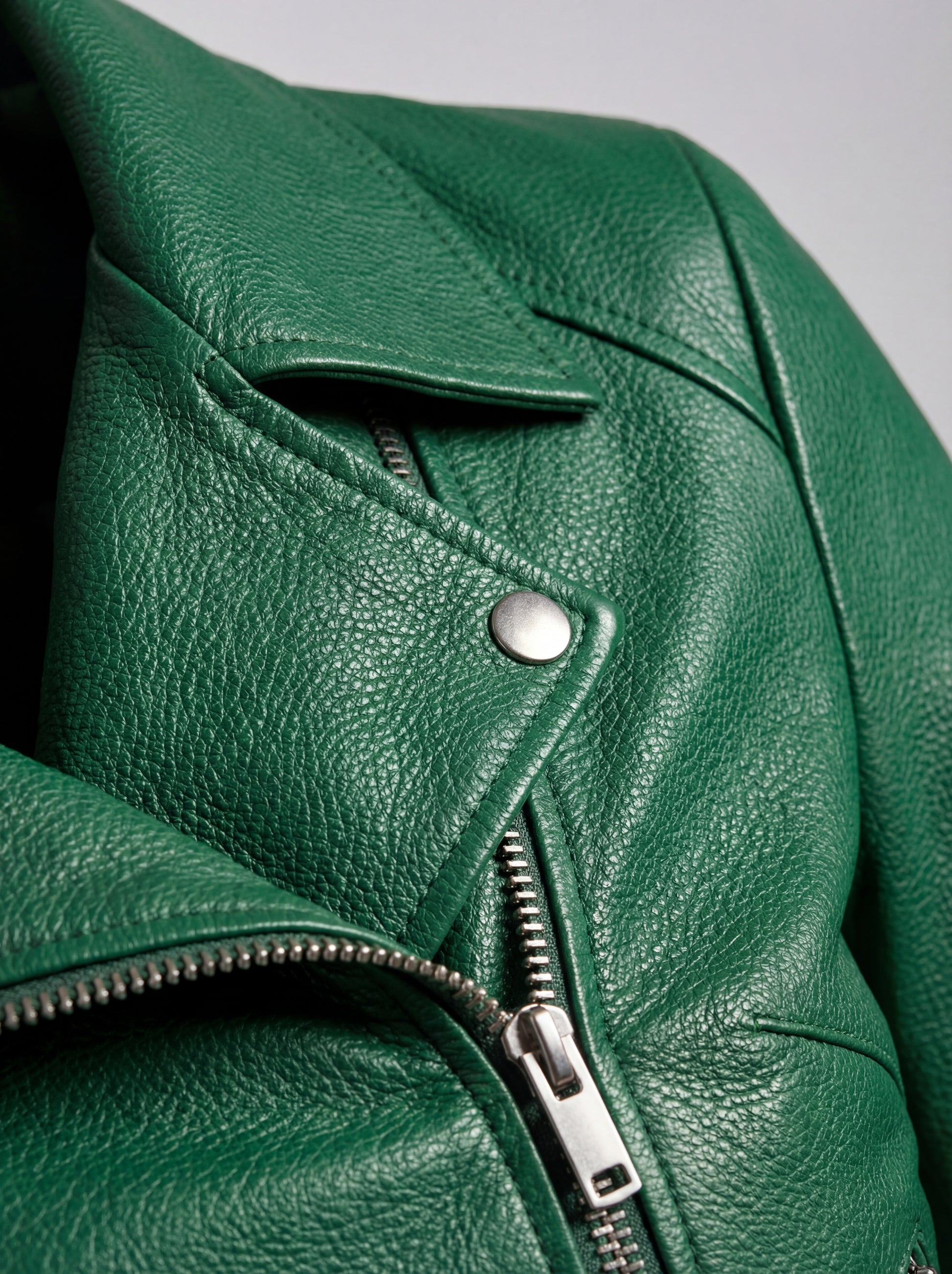 Macro shot of pebbled emerald green leather texture and silver snap button hardware on biker jacket. The Jade by Maverick Jacket.