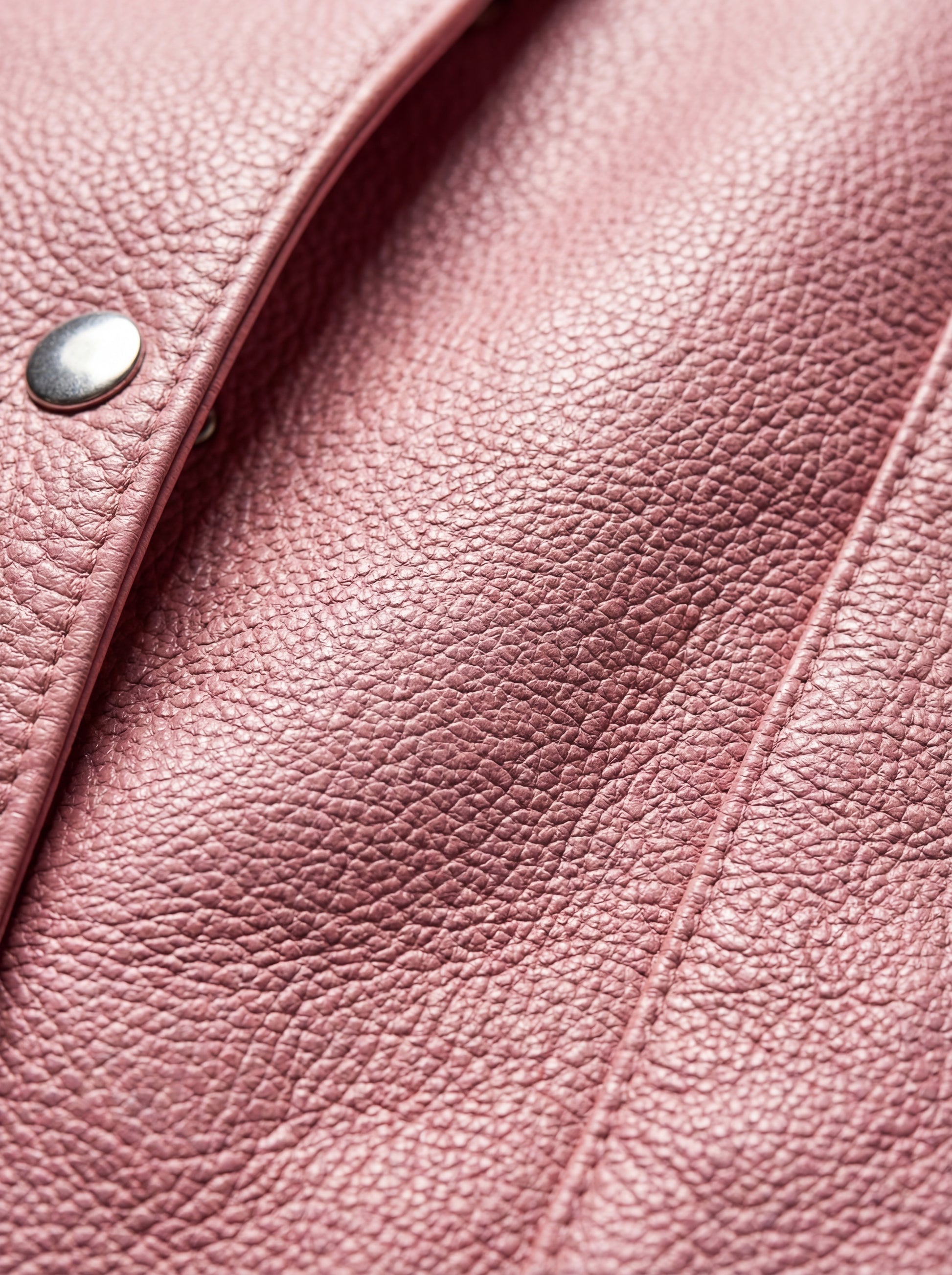 Macro shot of pebbled pink leather texture and silver snap button detail on vest. The Belle by Maverick Jacket.