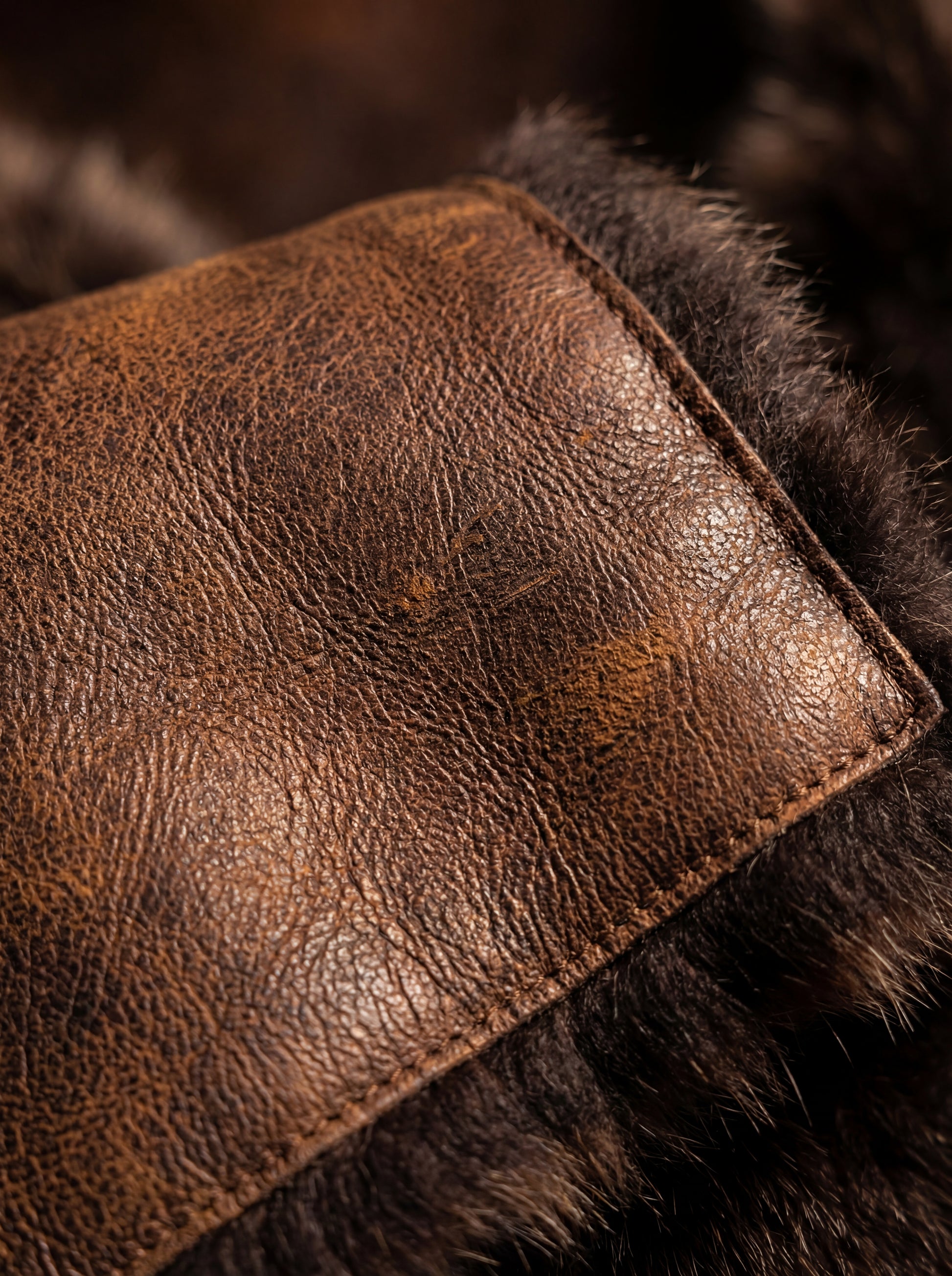 Macro shot of distressed brown leather texture and plush fur trim detail on vest. The Freya by Maverick Jacket.