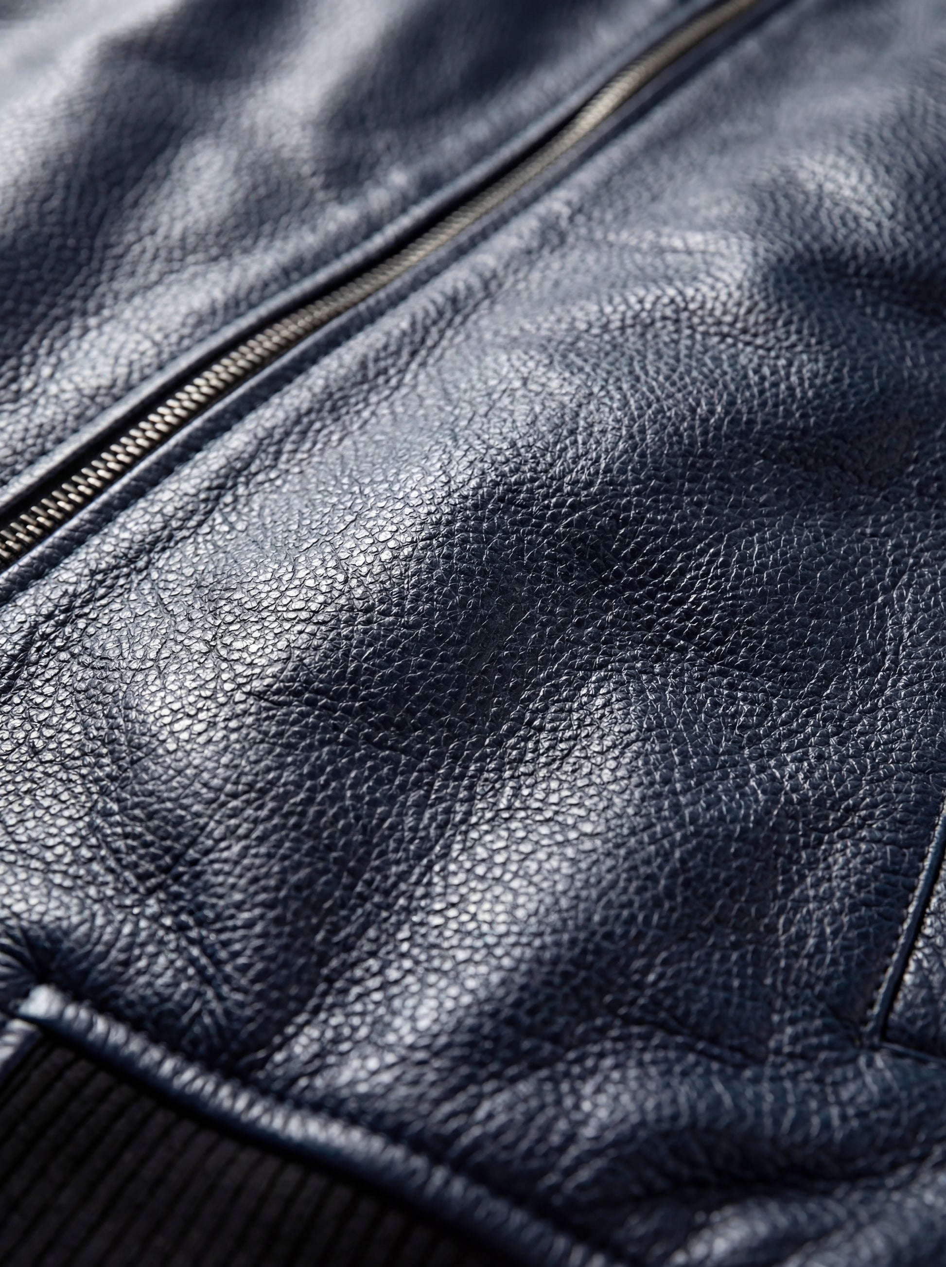 Macro shot of pebbled navy blue leather texture and silver zipper teeth on MA-1 bomber jacket. The Stratus by Maverick Jacket.