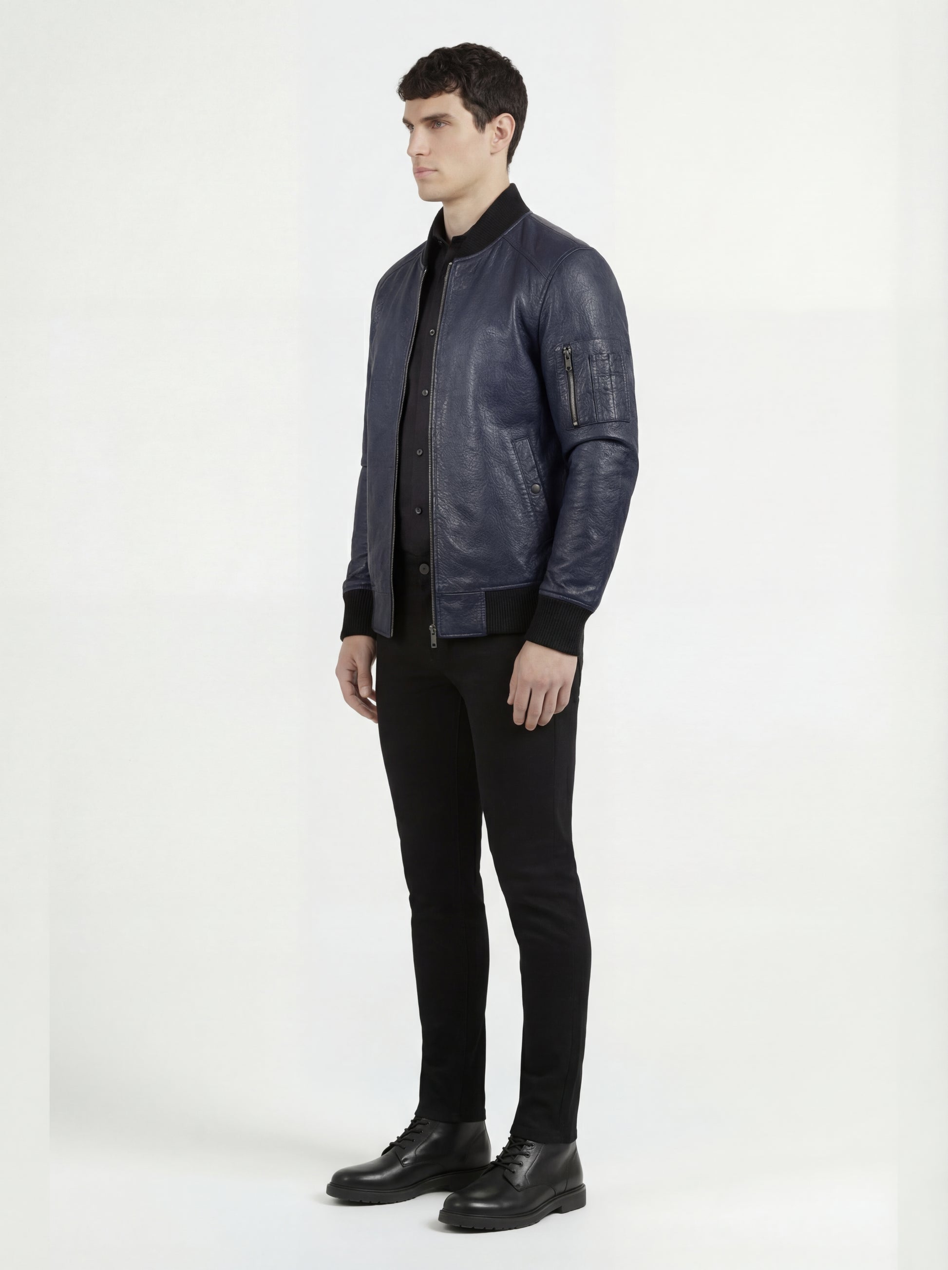 Side profile of Maverick Stratus navy blue leather bomber showing zippered sleeve utility pocket and straight torso fit. Maverick Jacket.
