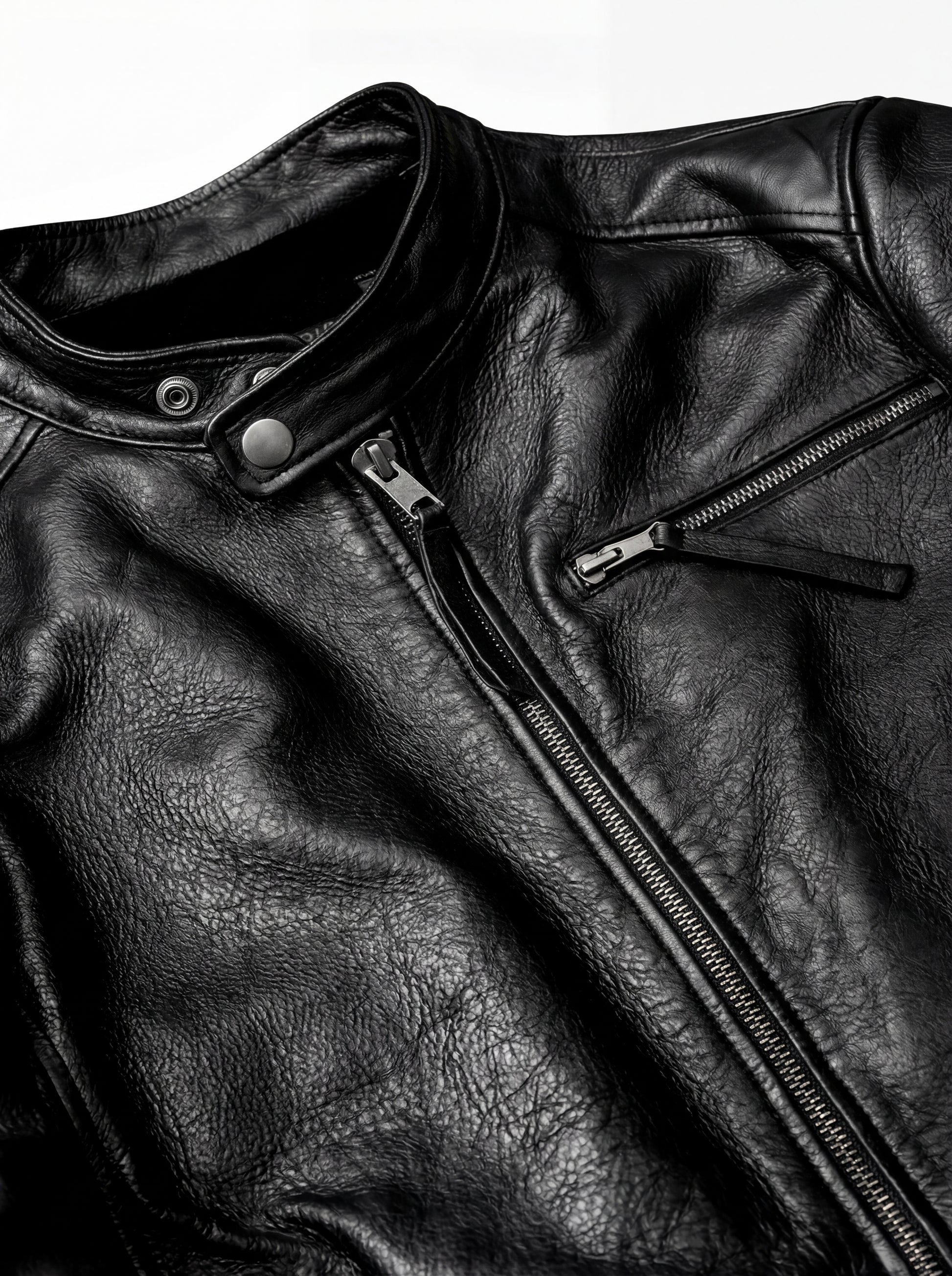 Macro shot of textured black leather grain and silver zipper hardware on cafe racer jacket. The Zenith by Maverick Jacket.