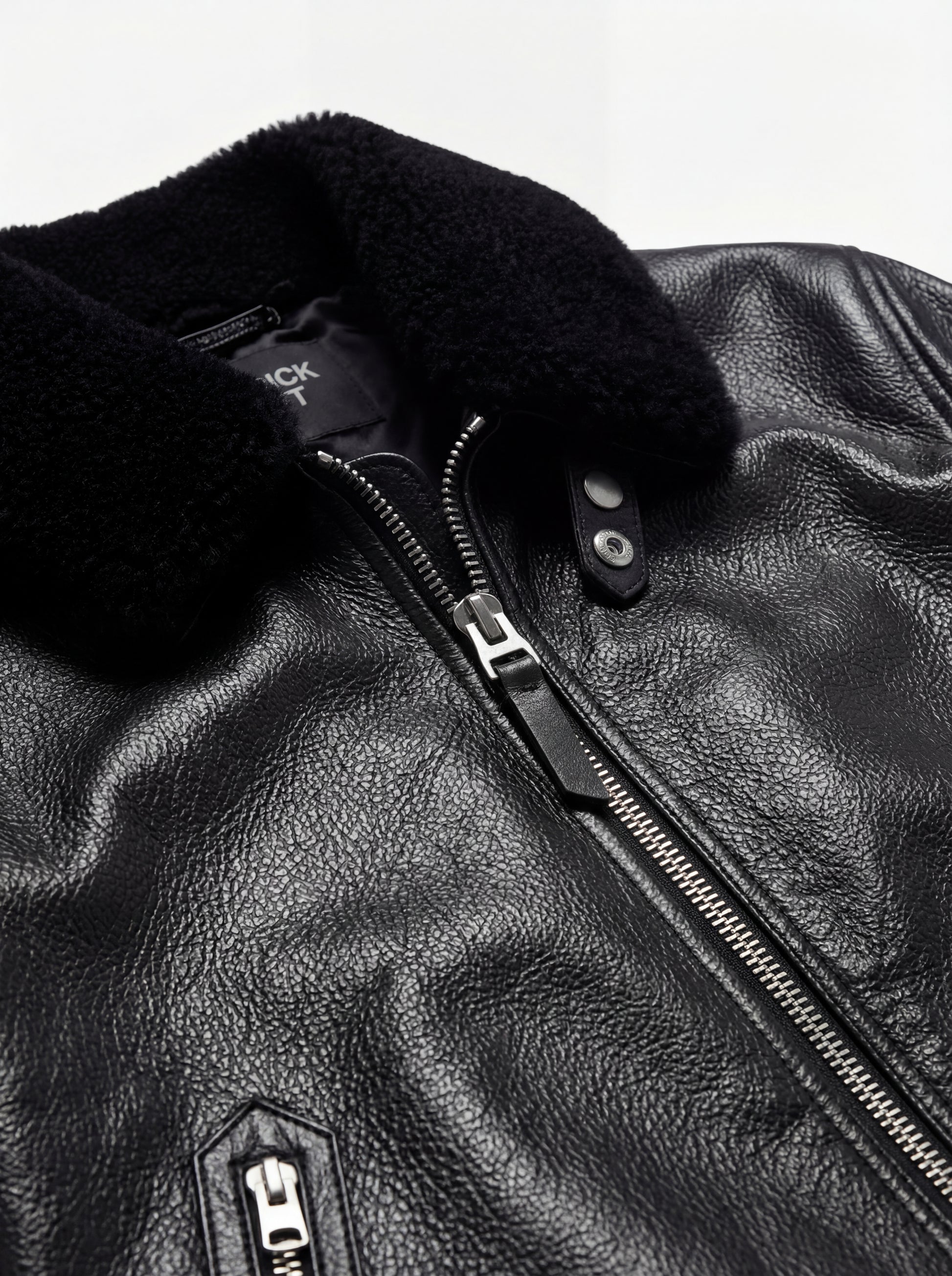 Macro shot of pebbled black leather texture and plush fur collar detail on Flight Jacket. The Phantom by Maverick Jacket.