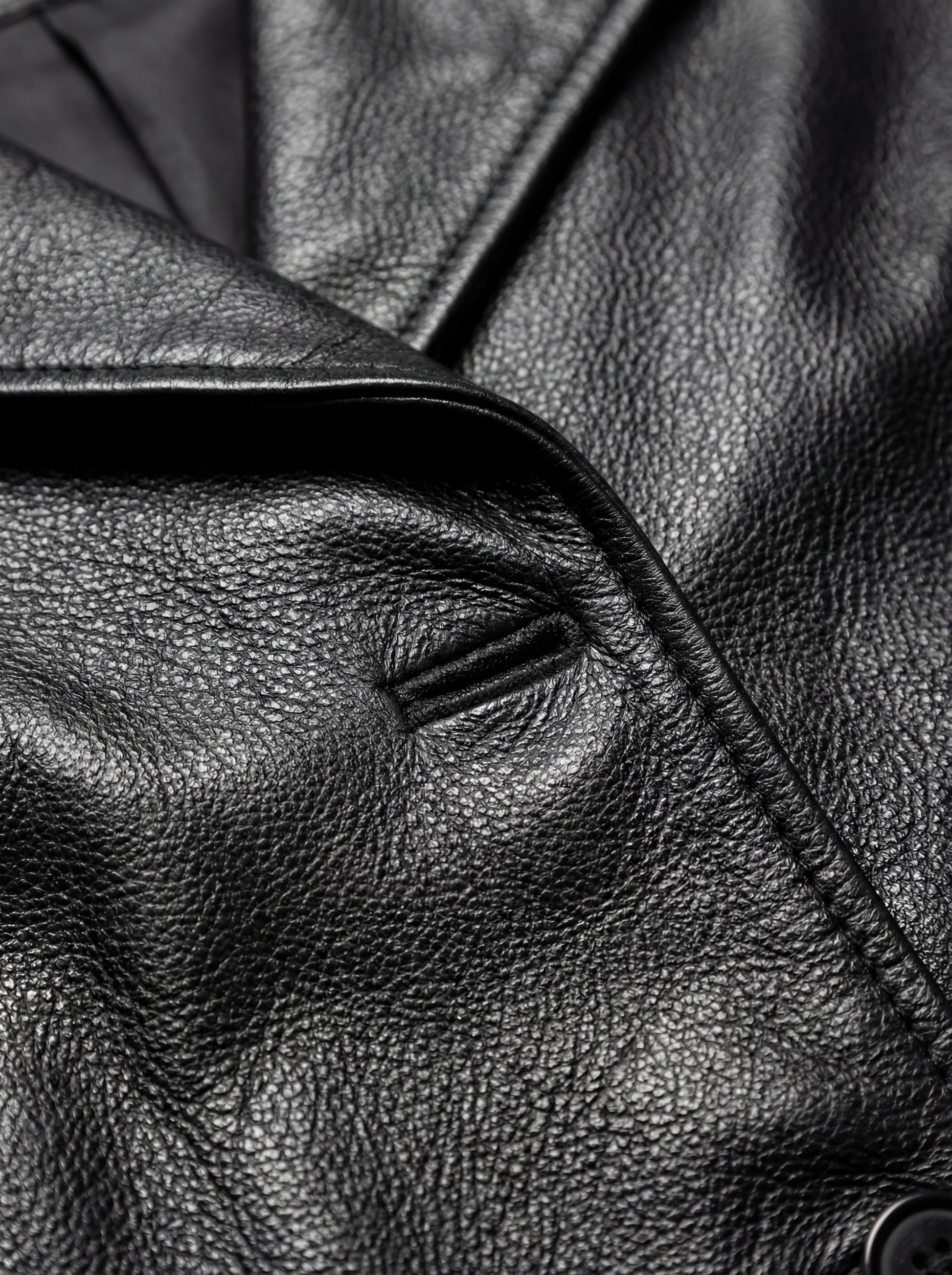 Macro shot of pebbled black leather texture and lapel buttonhole stitching on trench coat. Maverick Kensington.