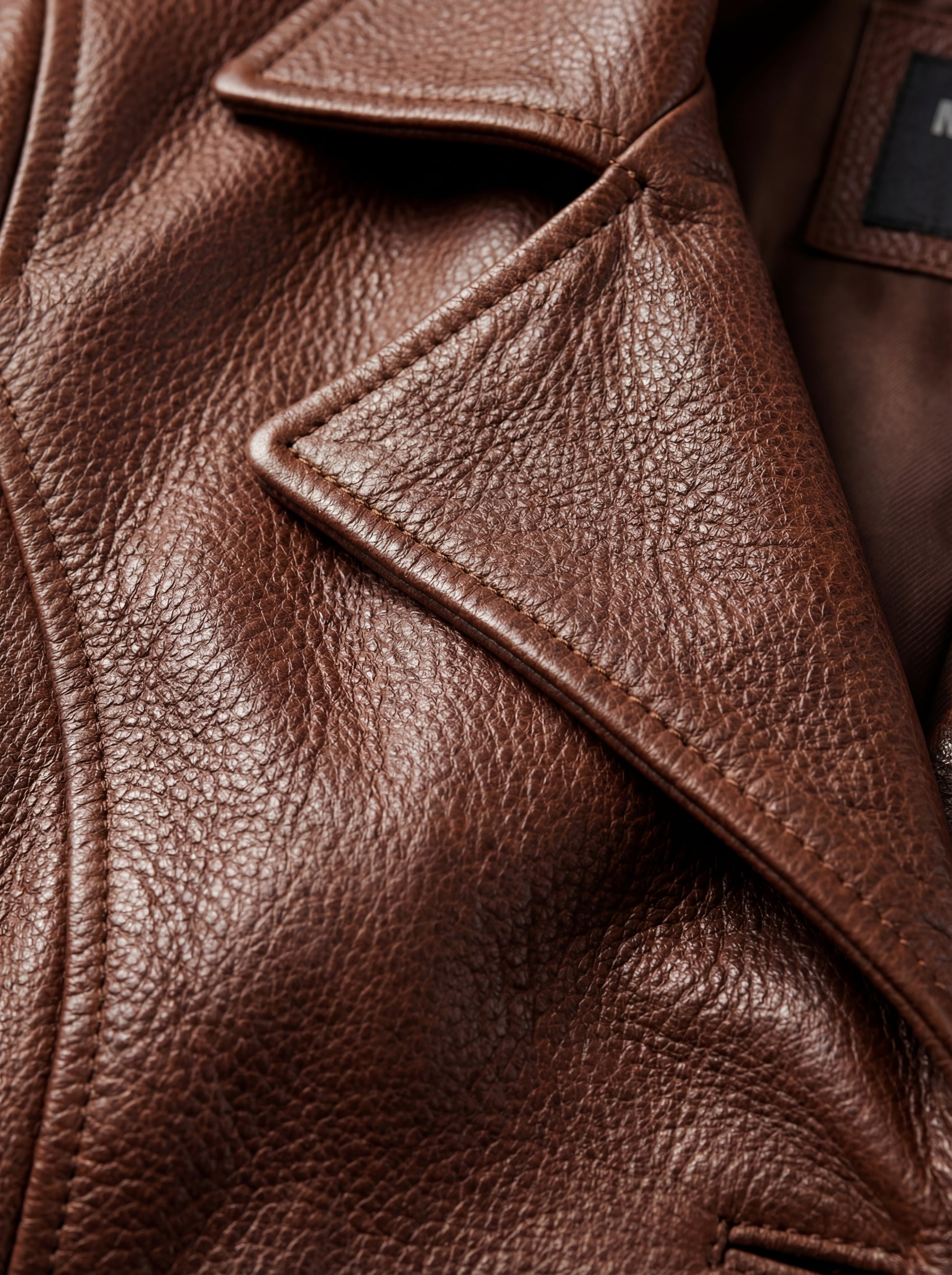 Macro shot of smooth cognac leather texture and tonal button hardware on walker coat. The York by Maverick Jacket.