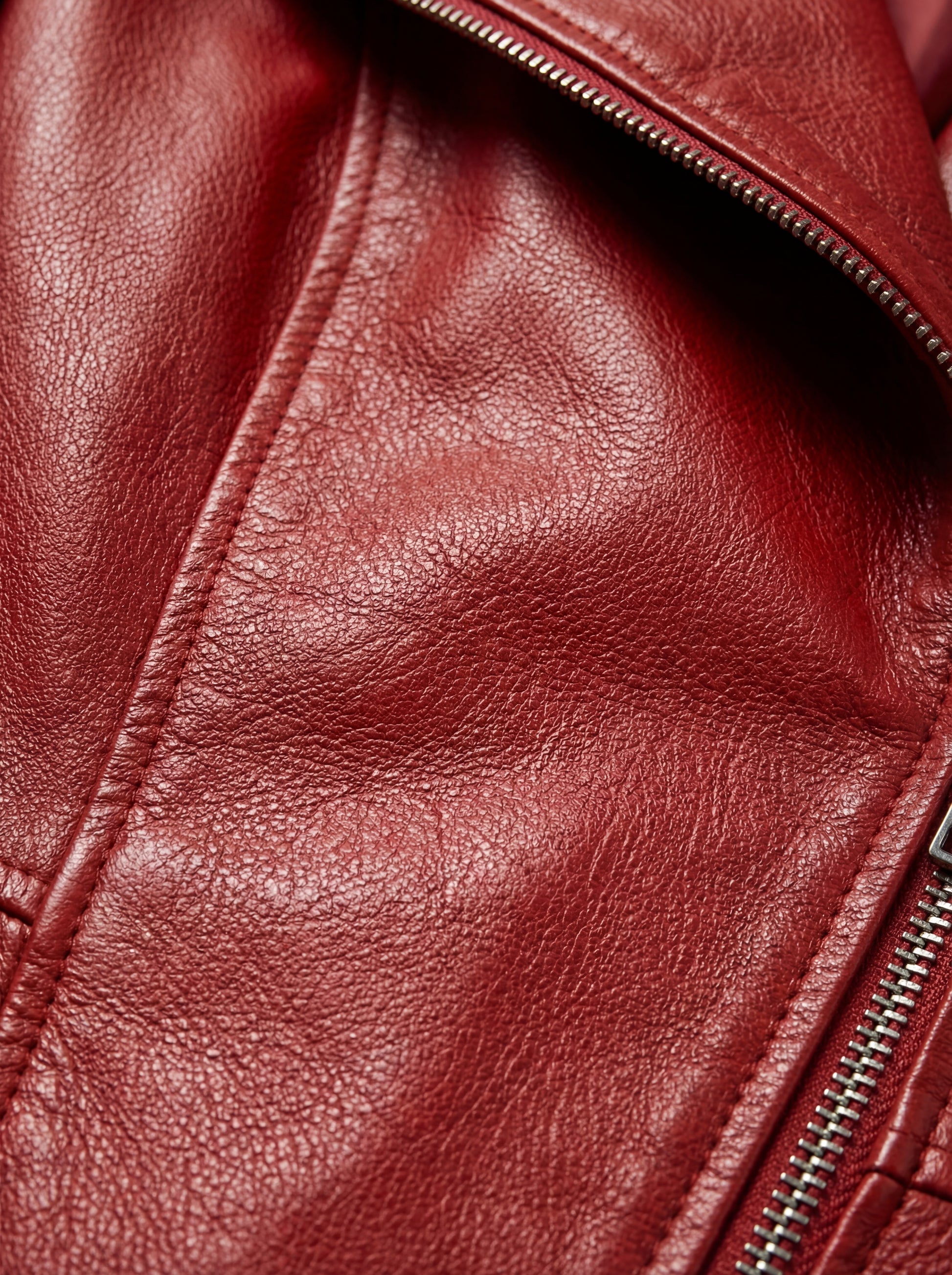 Macro shot of pebbled red leather texture and silver metal zipper teeth on peplum coat. Maverick Valencia.