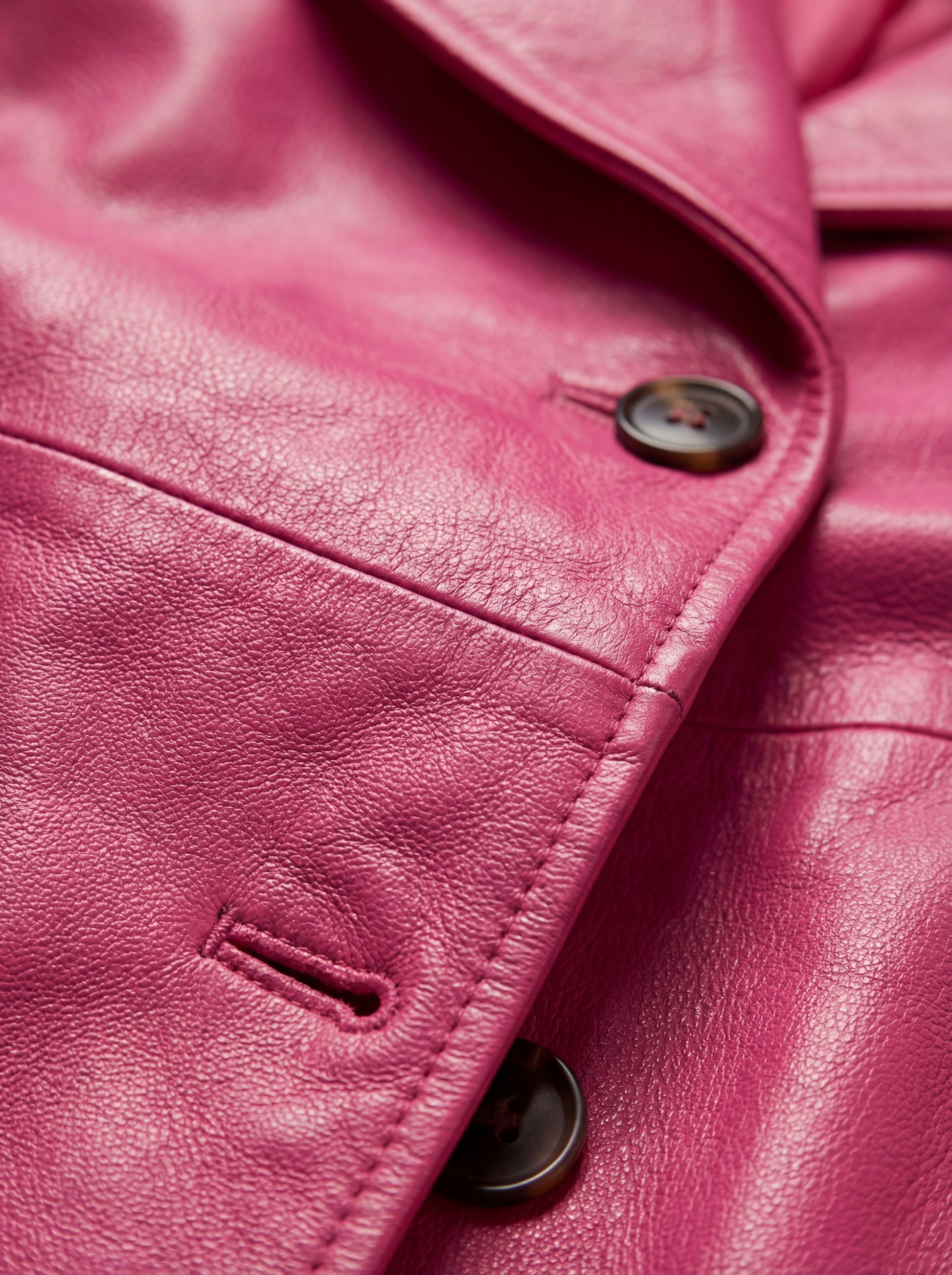 Macro shot of smooth pink leather texture and tonal button hardware on trench coat. The Eira is Maverick Jacket.