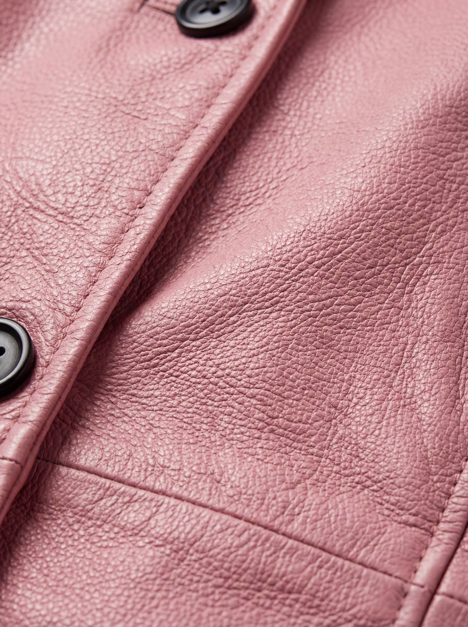 Macro shot of pebbled pink leather texture and black button hardware on walker coat. Maverick Camden.
