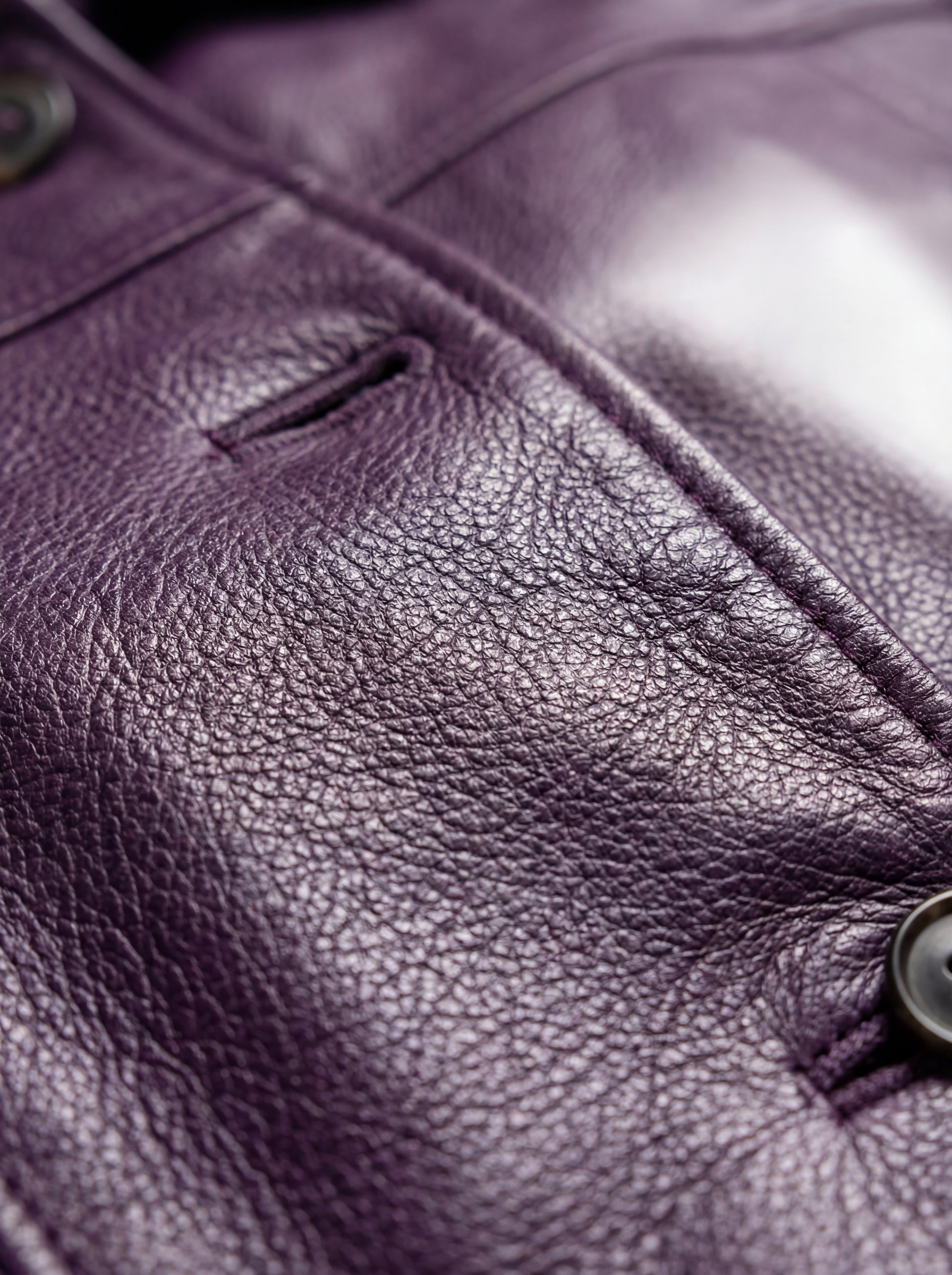 Macro shot of pebbled purple leather texture and buttonhole detail on walker coat. Maverick Helena.