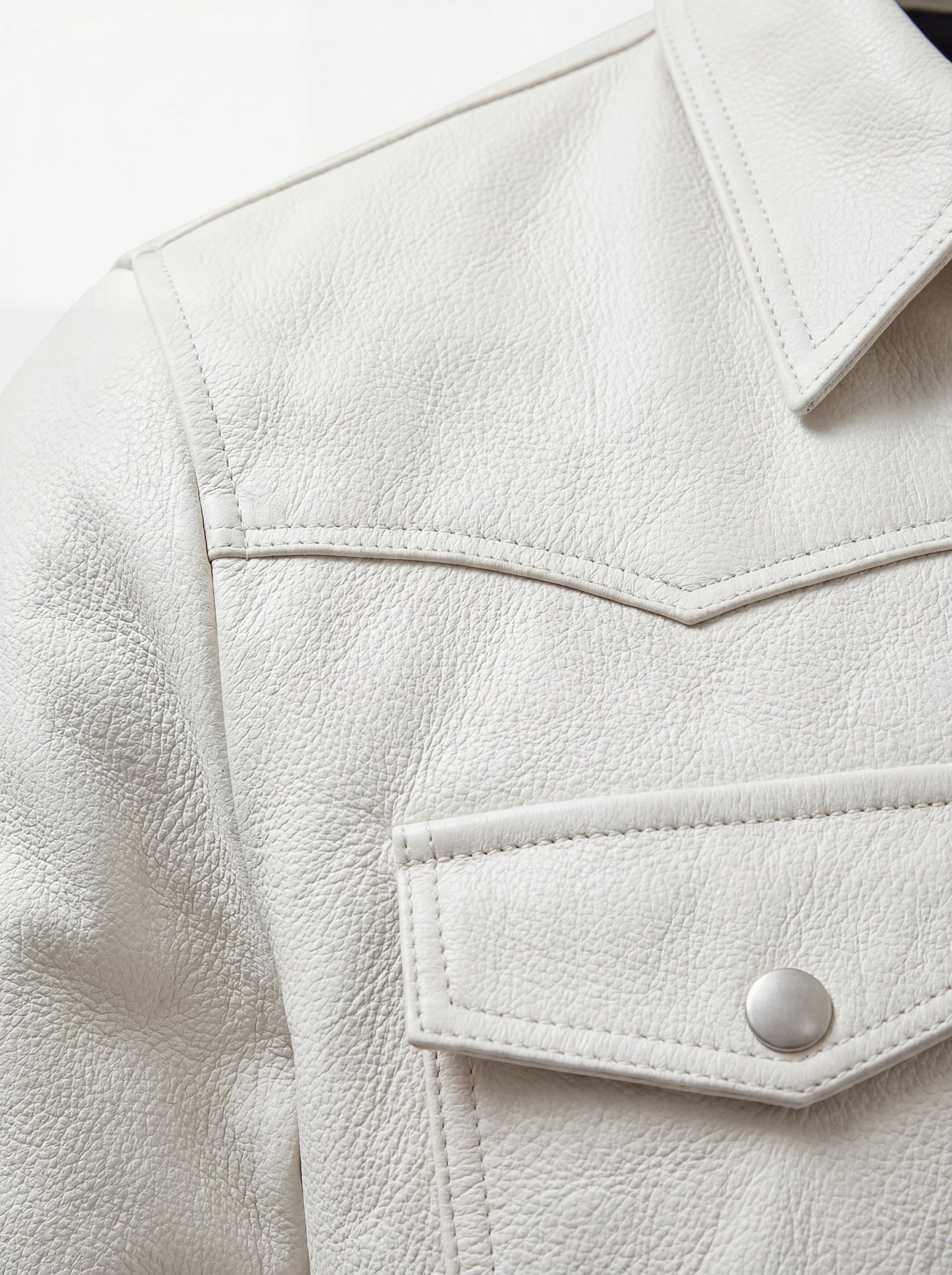 Macro shot of grained off-white leather texture and silver snap button detail on western shirt. The Tiernan by Maverick Jacket.