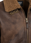 Macro shot of pebbled brown leather texture and buckle strap hardware on shearling cuff. The Declan by Maverick Jacket.