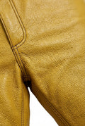 Macro shot of yellow leather texture and front pocket rivet detail on trousers. Maverick Huxley.
