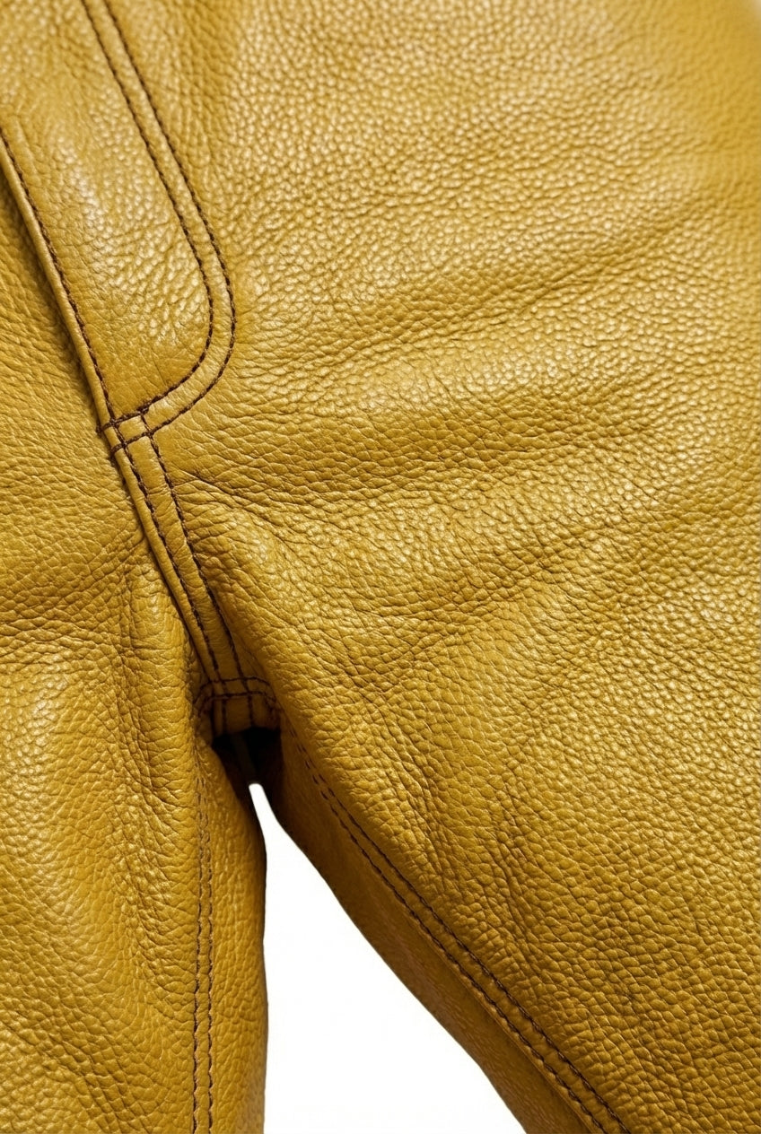 Macro shot of yellow leather texture and front pocket rivet detail on trousers. Maverick Huxley.