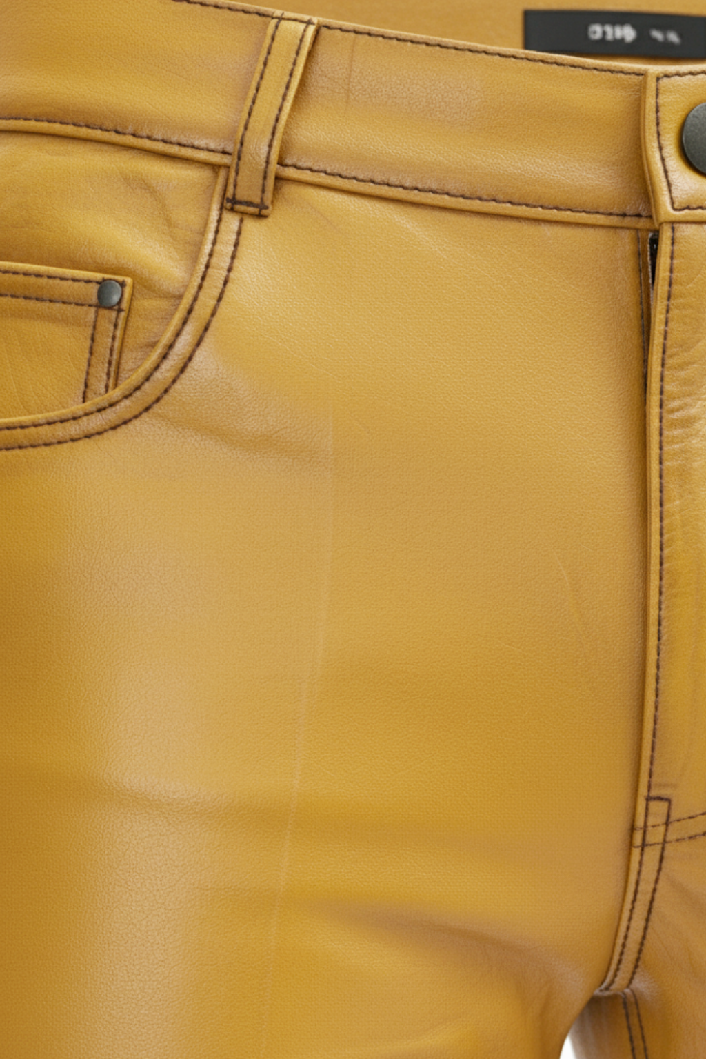 Macro shot of grained yellow leather texture and reinforced inseam stitching on trousers. The Huxley by Maverick Jacket.