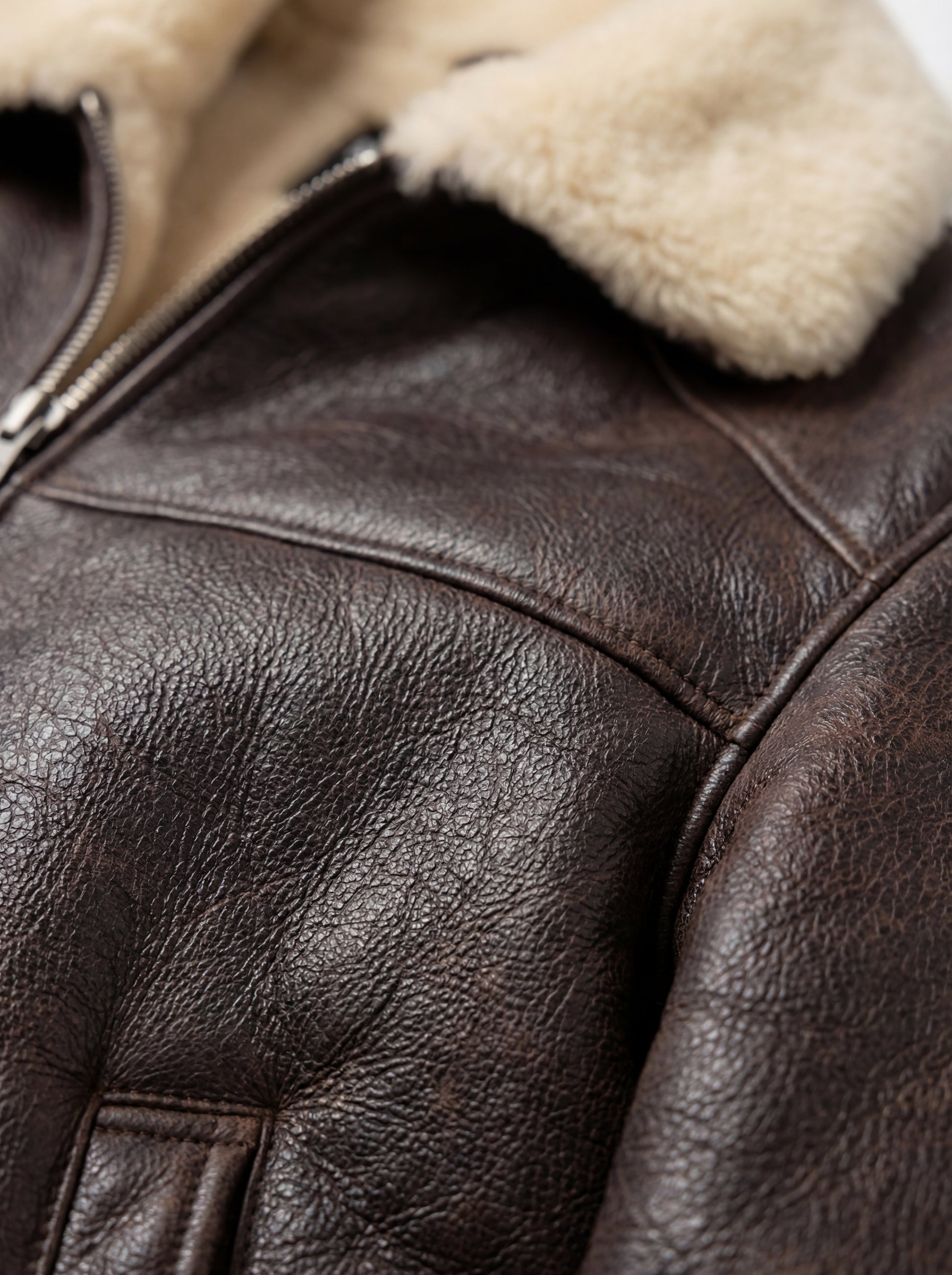 Macro shot of dark brown pebbled leather grain and cream shearling collar texture on aviator jacket. The Nomad by Maverick Jacket.