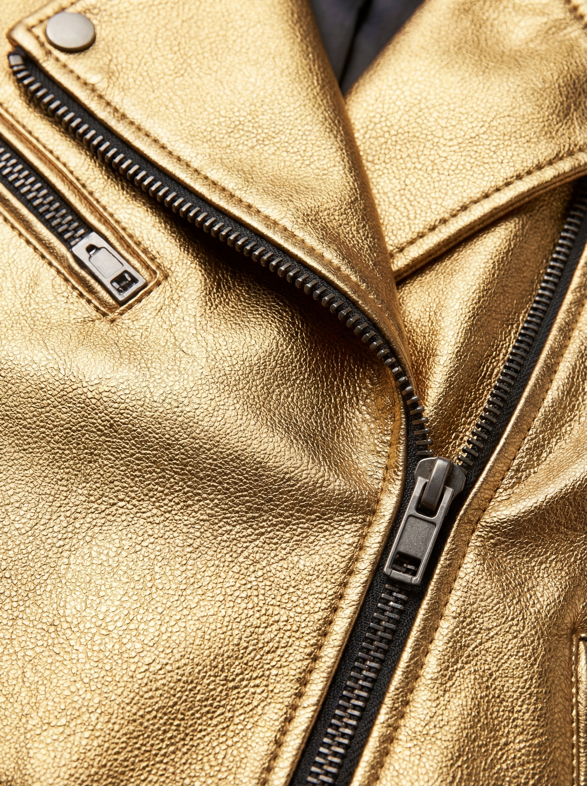 Macro shot of metallic gold leather texture and silver zipper lapel detail on biker jacket. The Aurora by Maverick Jacket.