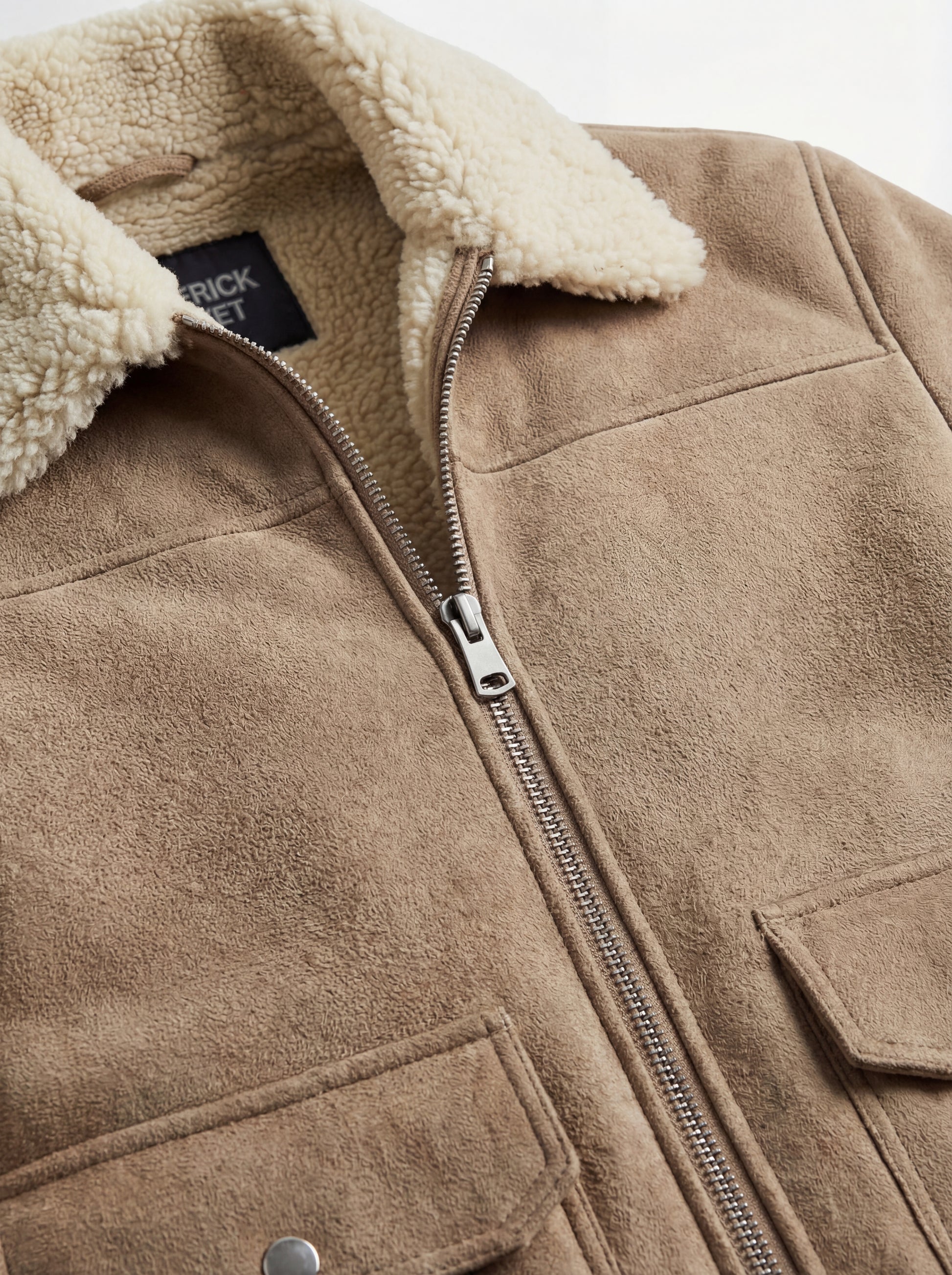 Macro shot of soft beige suede texture and silver zipper hardware on shearling jacket. The Dune by Maverick Jacket.