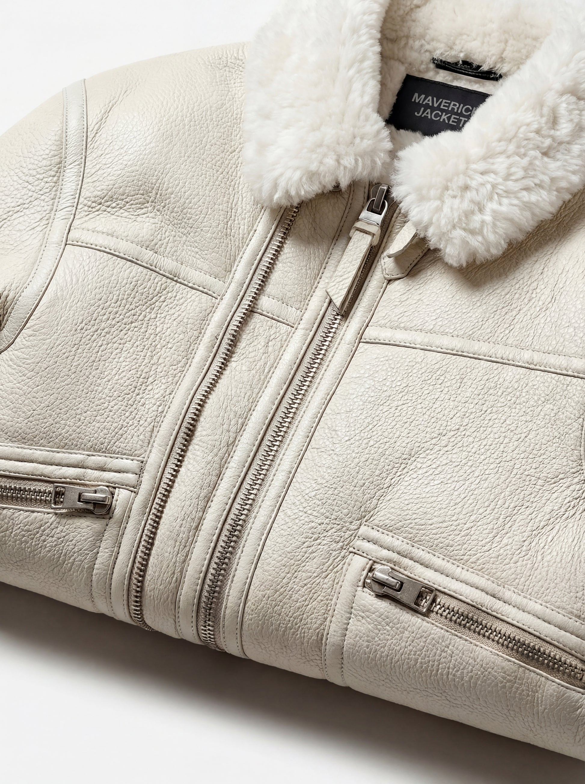 Macro shot of white pebbled leather texture and silver metal zipper hardware on shearling jacket. The Summit by Maverick Jacket.