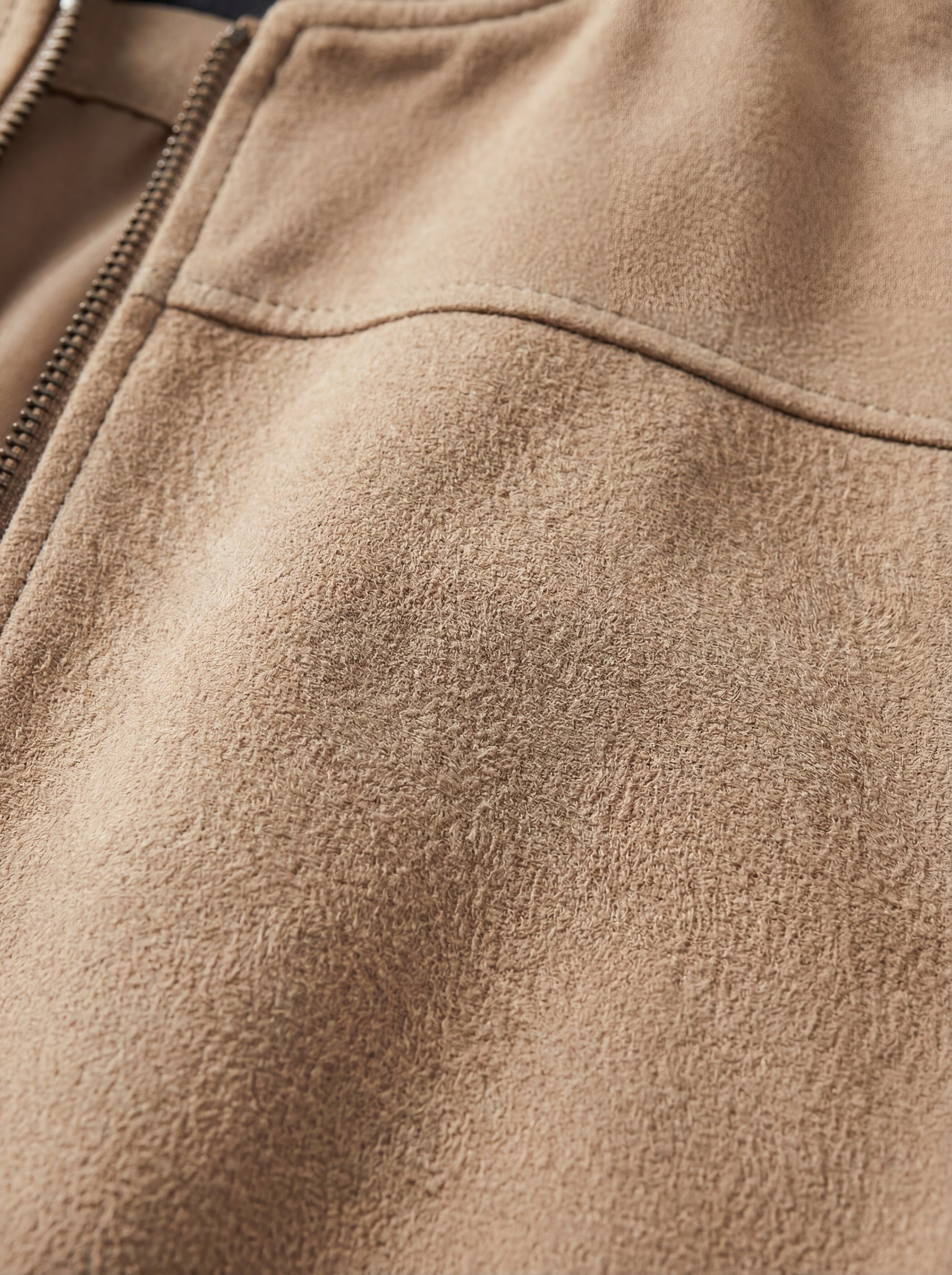 Macro shot of soft tan suede texture and metal zipper hardware on bomber jacket. The Cian by Maverick Jacket.