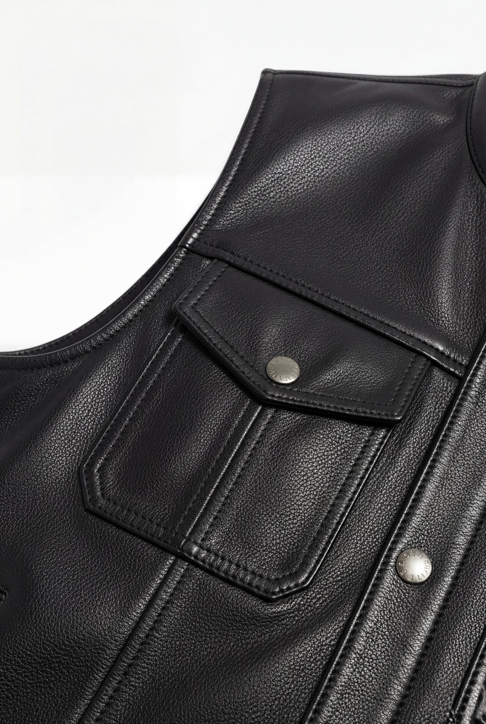 Macro shot of smooth black leather texture and metal hardware details on utility vest. The Arlo by Maverick Jacket.