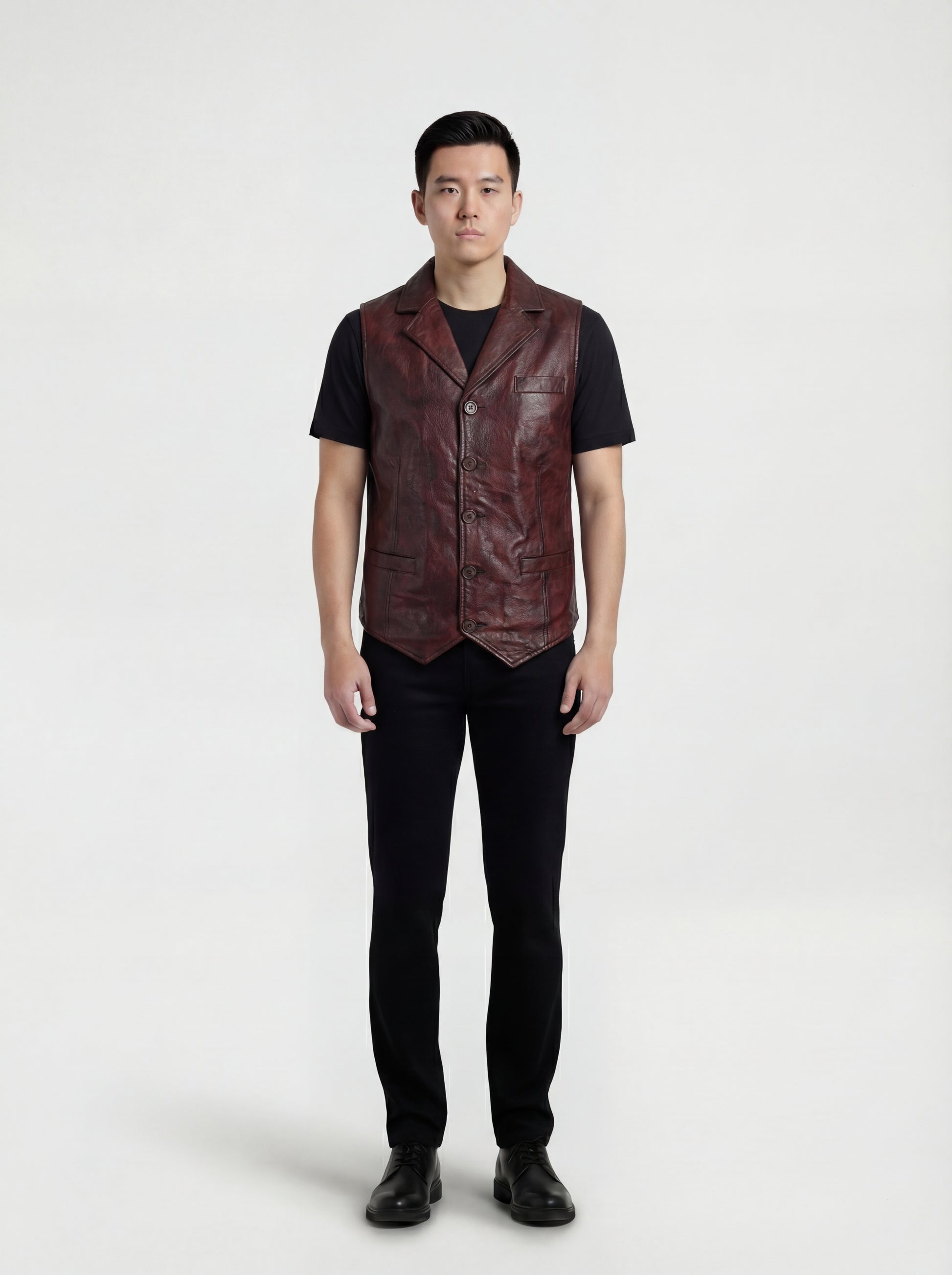 Male model wearing Maverick Rook leather button vest, regular fit, styled over a black hoodie with dark indigo denim jeans. Maverick Jacket.