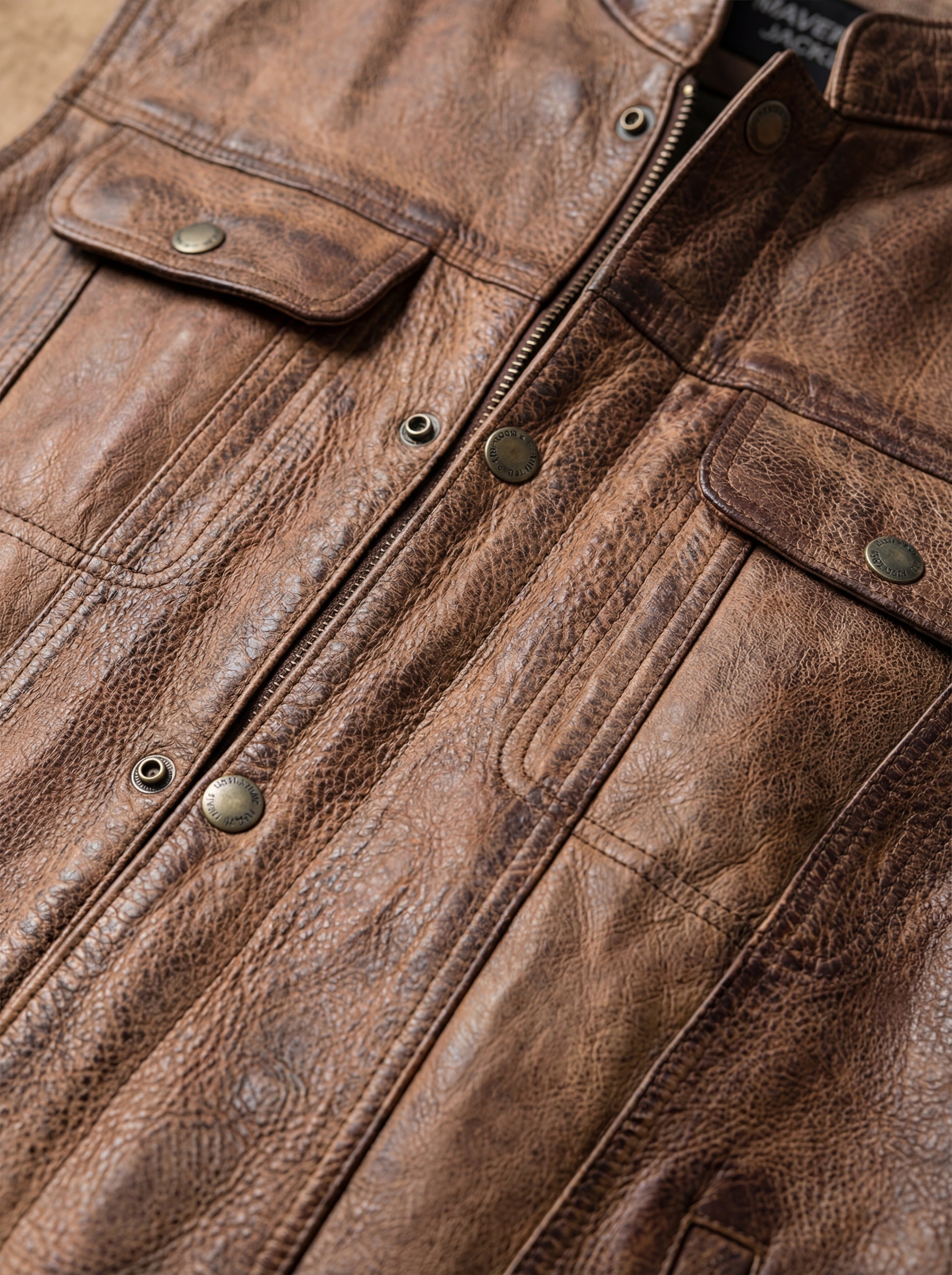 Macro shot of worn distressed leather texture and antique brass hardware on vest. The Drifter by Maverick Jacket.