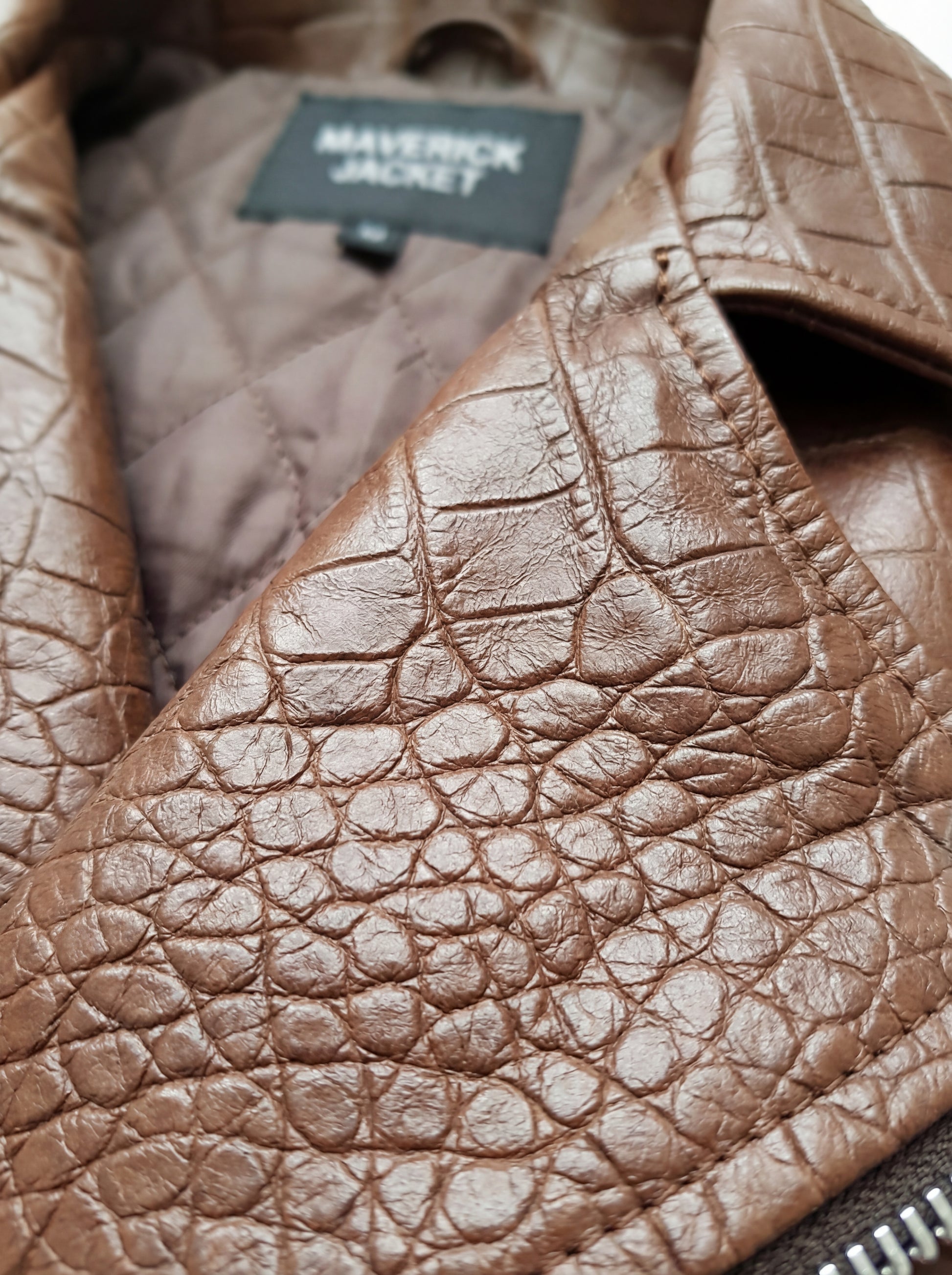 Macro shot of textured croc-embossed leather skin and heavy-duty silver zipper on biker vest. The Drake by Maverick Jacket.