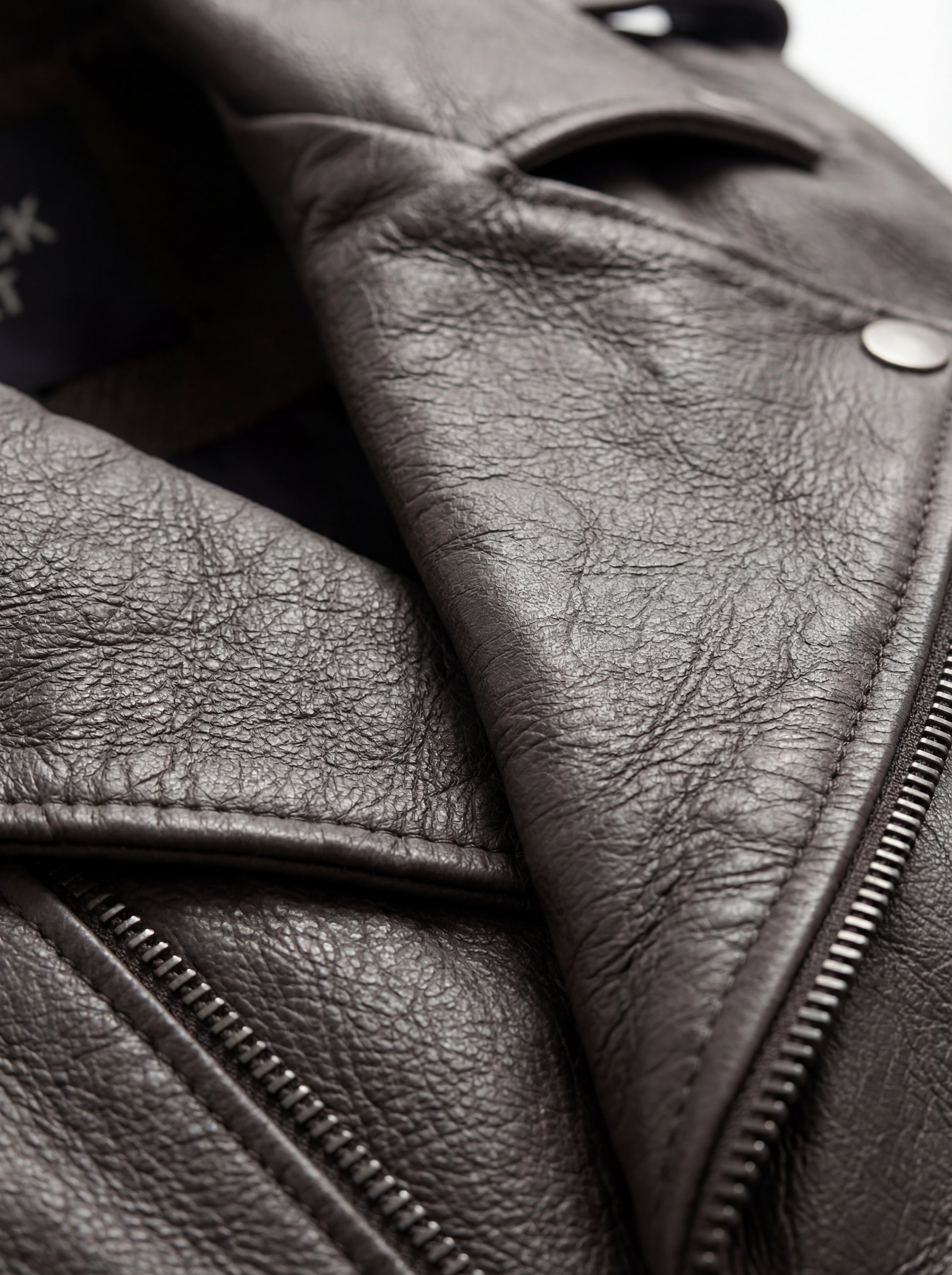 Macro shot of smooth grey leather texture and heavy-duty silver zipper hardware on biker vest. The Vulcan by Maverick Jacket.