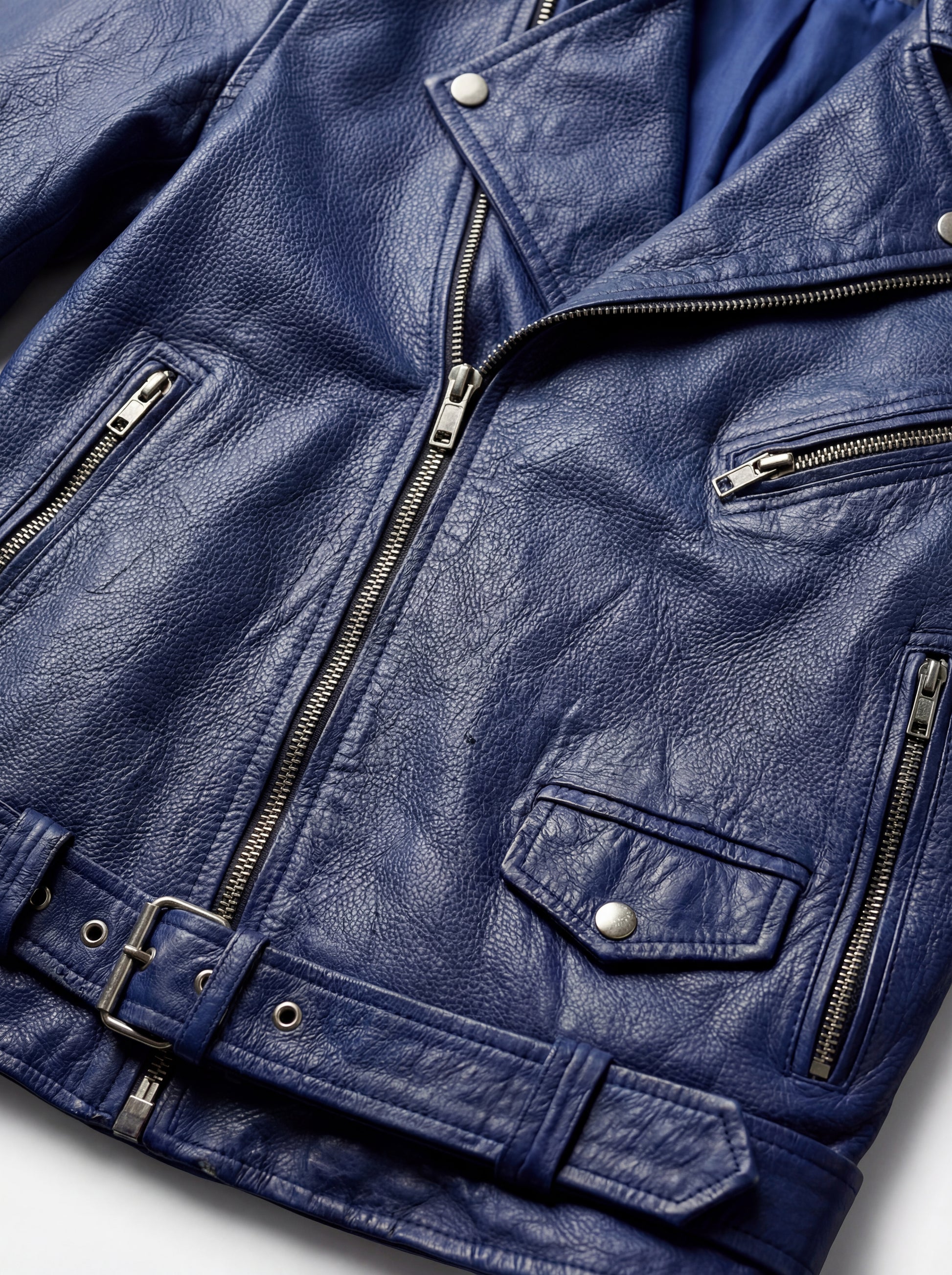 Macro shot of textured blue leather grain and silver asymmetrical zipper hardware on biker jacket. The Vector by Maverick Jacket.