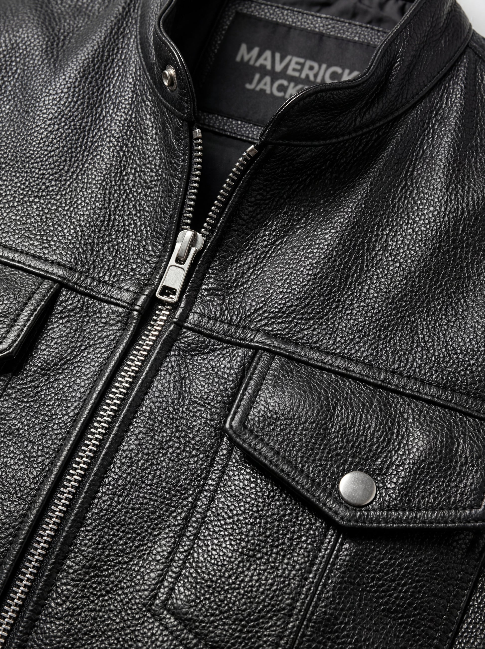 Macro shot of smooth black leather texture and heavy-duty silver zipper hardware on biker vest. The Riot by Maverick Jacket.
