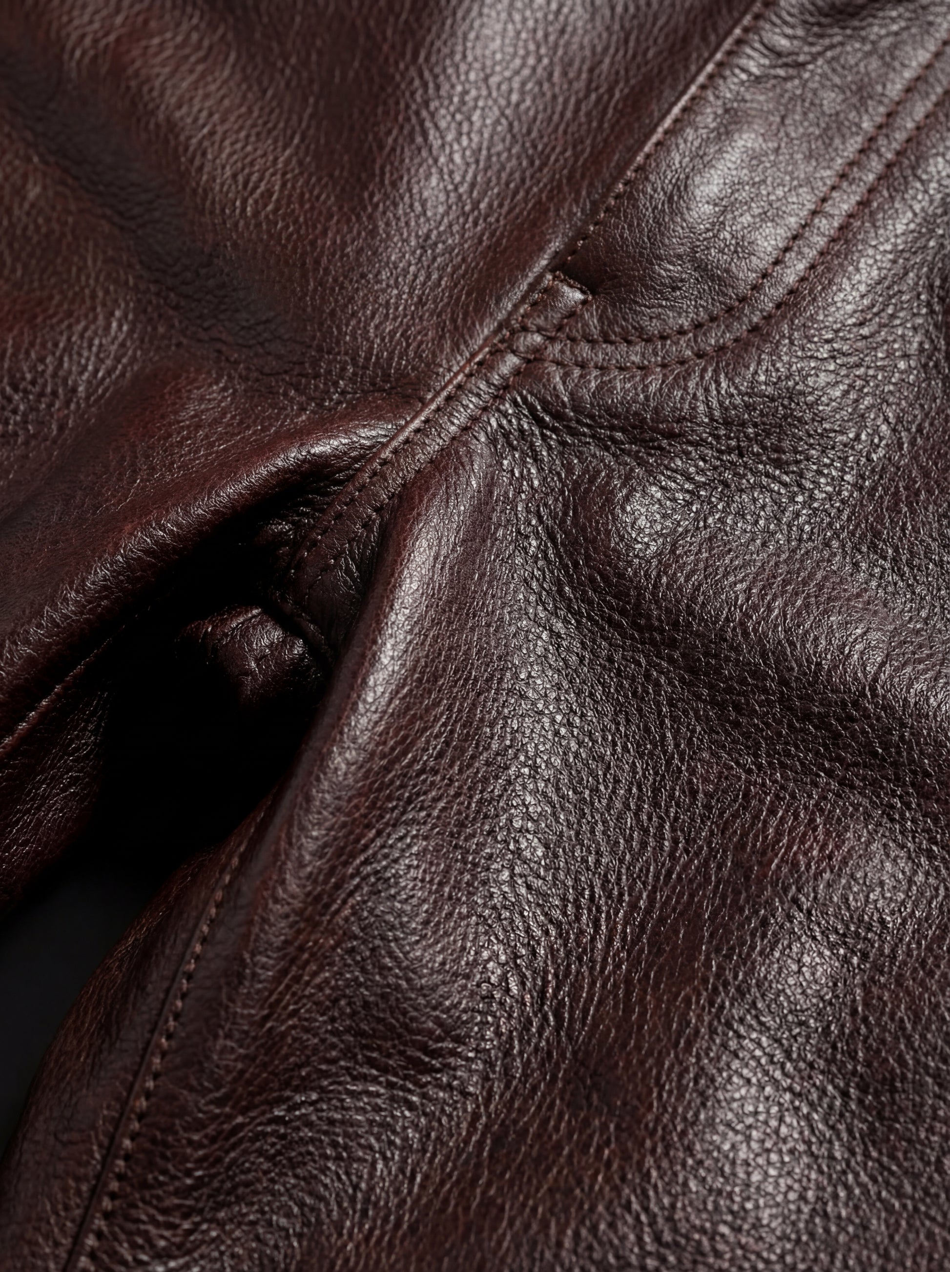 Macro shot of grained leather texture and heavy reinforced stitching on trousers. The Kade by Maverick Jacket.