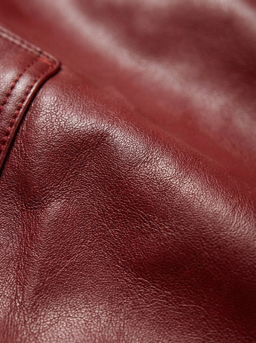 Macro shot of grained red leather texture and reinforced stitching on cargo pocket flap. The Cassian by Maverick Jacket.