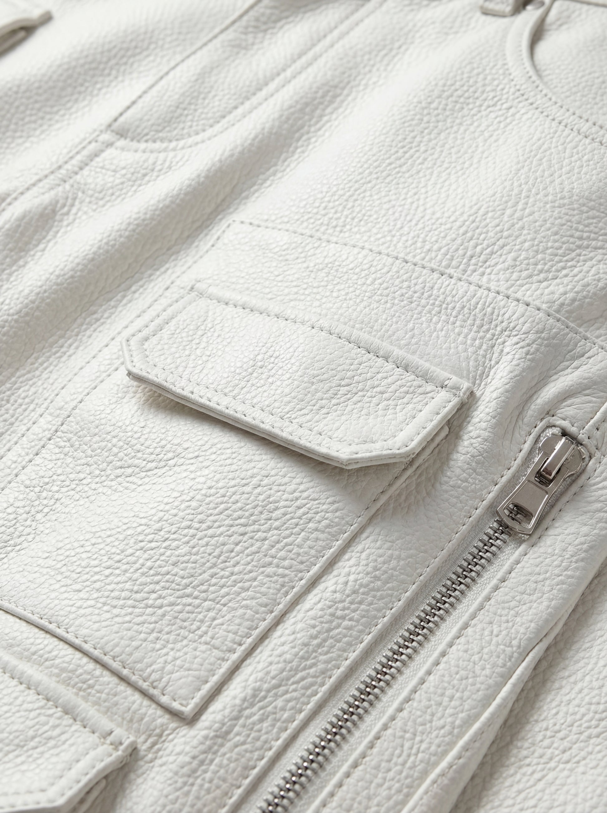 Macro shot of bone white pebbled leather texture and silver zipper hardware on cargo trousers. The Spectre by Maverick Jacket.
