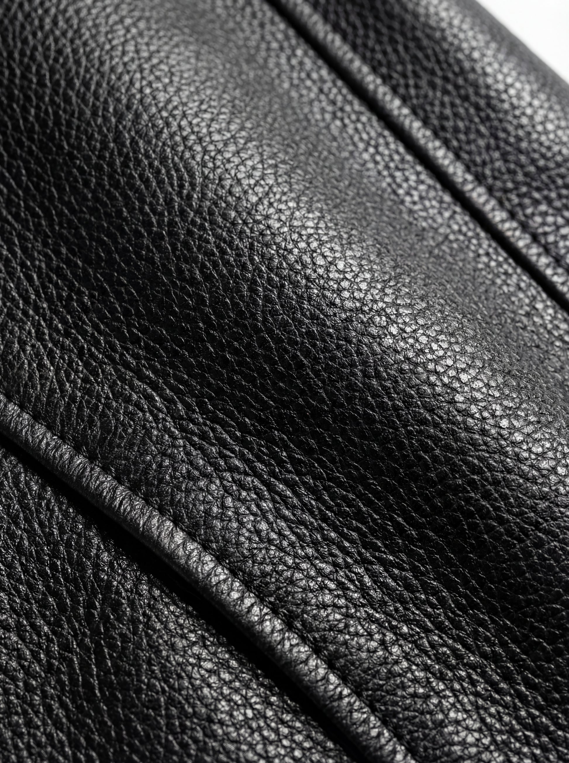 Macro shot of pebbled Onyx leather texture and reinforced button stitching on trench coat. The Sovereign by Maverick Jacket.