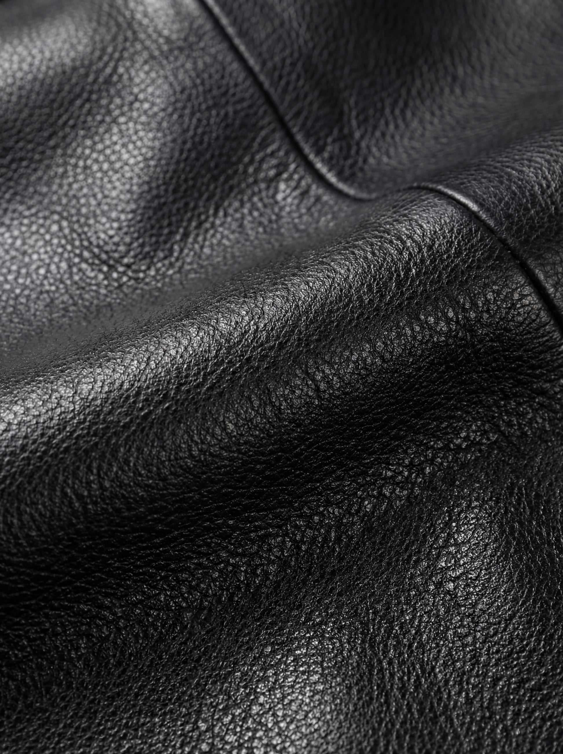 Macro shot of pebbled black leather texture and reinforced seam stitching on car coat. The Hawk by Maverick Jacket.