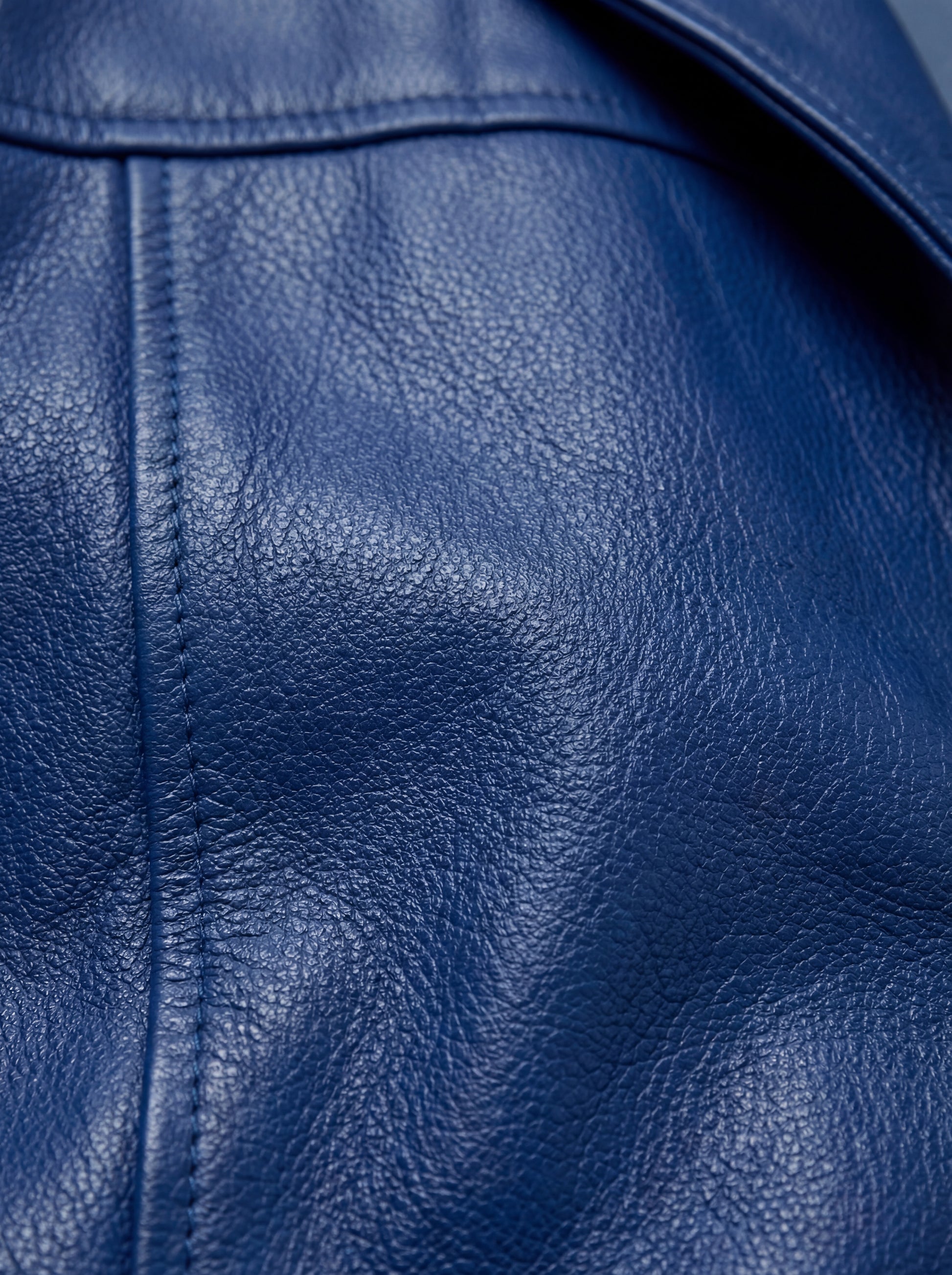 Macro shot of pebbled blue leather texture and reinforced seam stitching on Mac Coat. The Regent by Maverick Jacket.