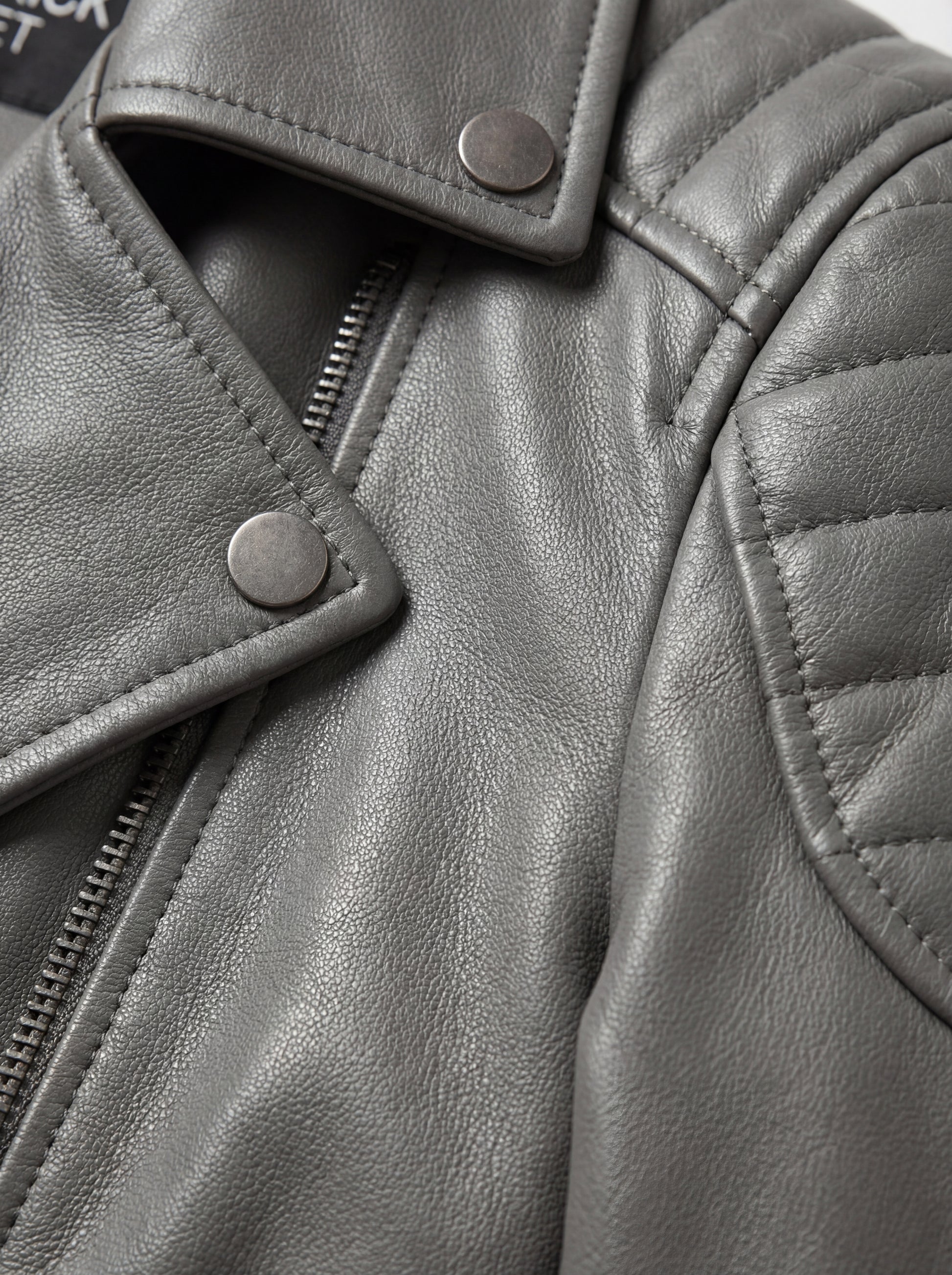 Macro shot of grained grey leather texture and silver snap button lapel detail on biker jacket. The Morrigan by Maverick Jacket.