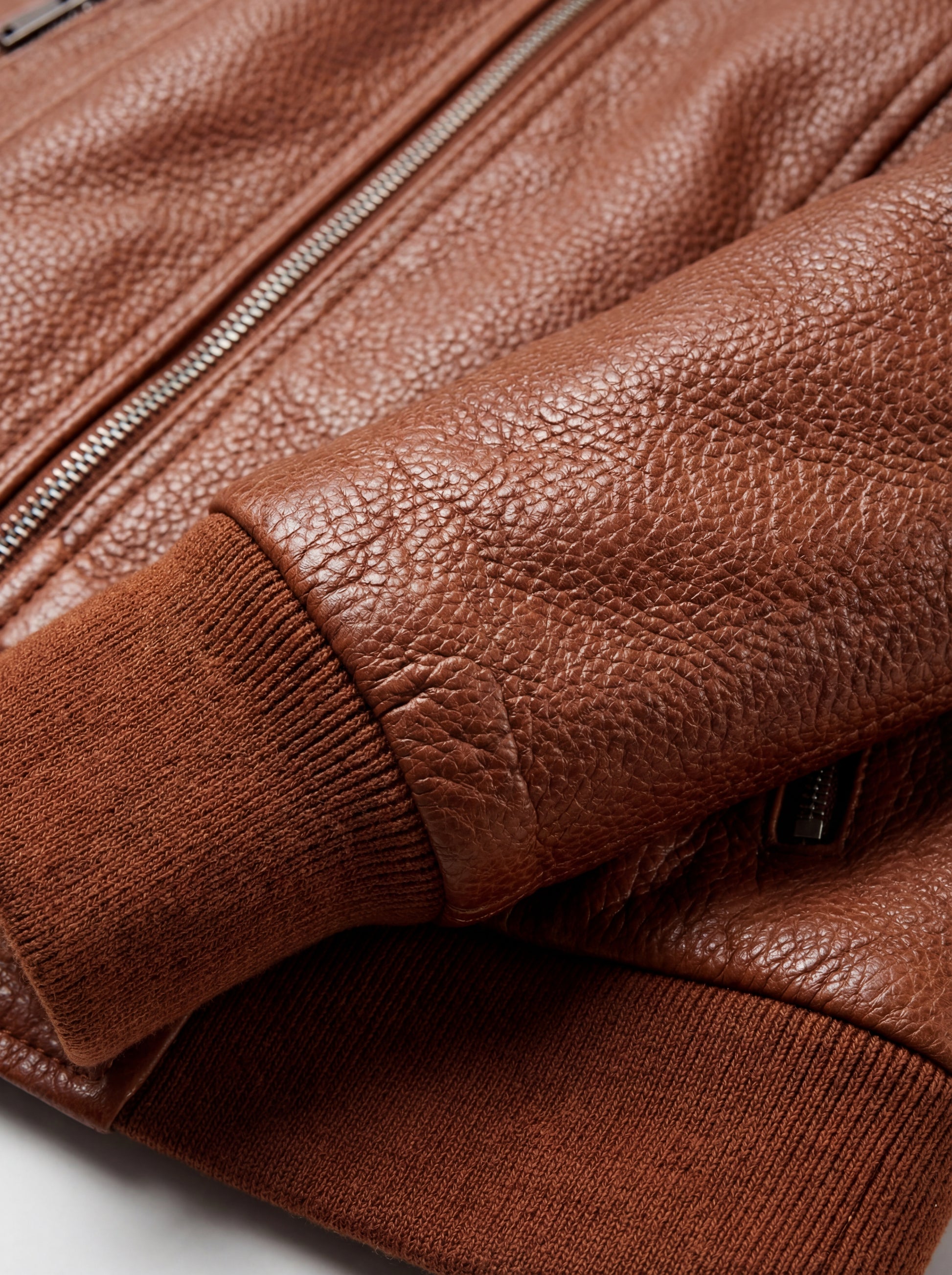Macro shot of pebbled tan leather texture and ribbed knit cuff detail on bomber jacket. The Blair by Maverick Jacket.