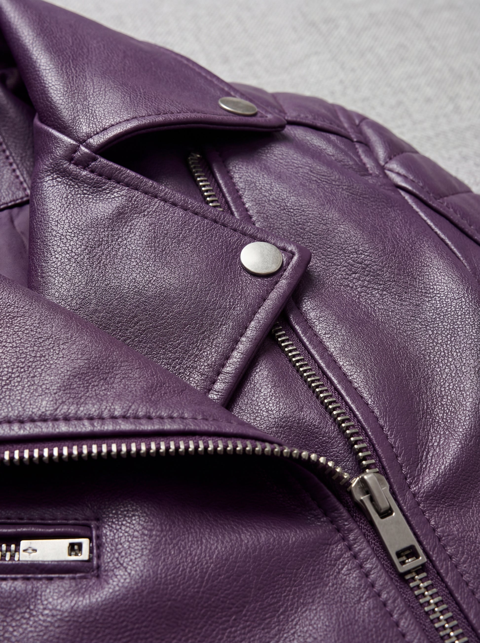 Macro shot of grained purple leather texture and silver snap button lapel detail on biker jacket. The Iris by Maverick Jacket.