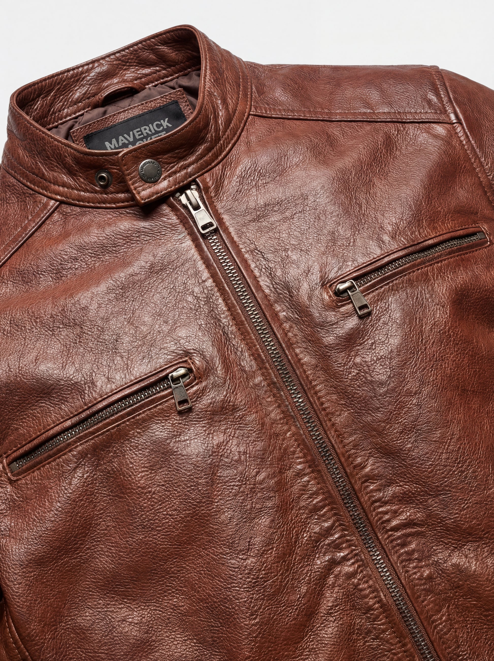 Macro shot of textured brown leather grain and gunmetal zipper hardware on cafe racer jacket. The Meridian by Maverick Jacket. 