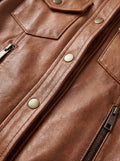 Macro shot of grained tan leather texture and antique brass snap button detail on utility jacket. The Quinn by Maverick Jacket.