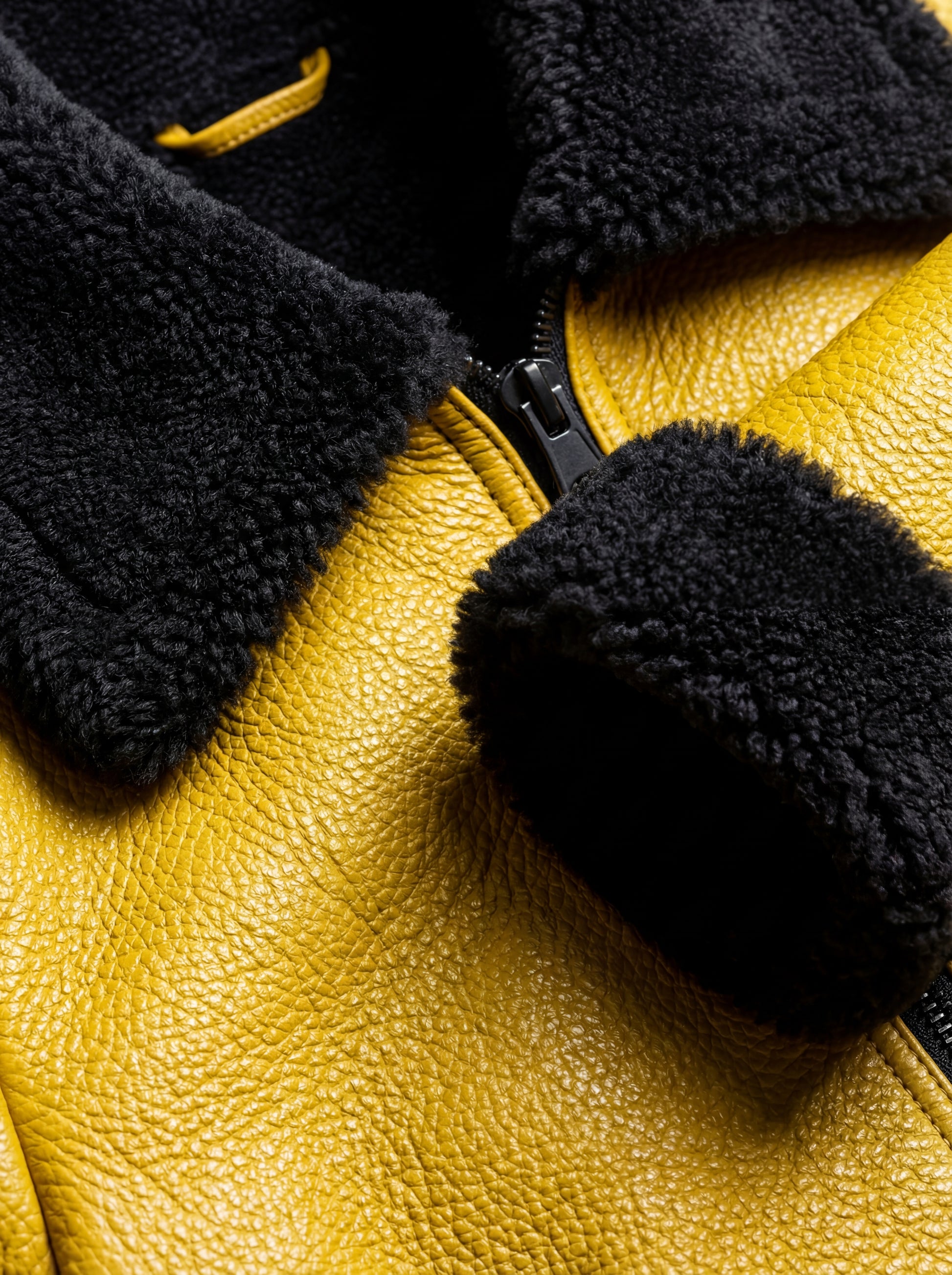 Macro shot of yellow pebbled leather grain and dense black shearling wool texture on collar. The Voltage by Maverick Jacket.