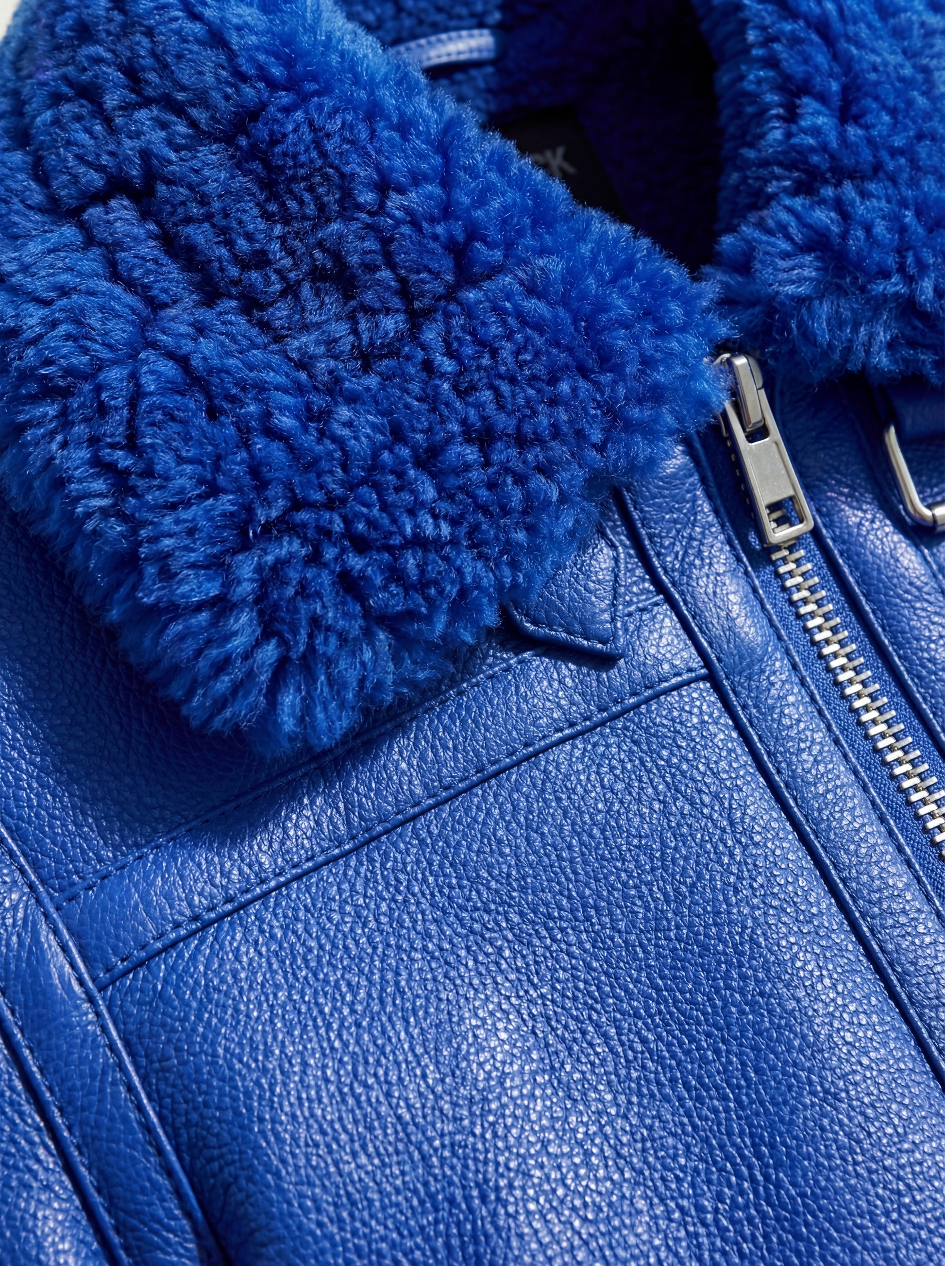 Macro shot of electric blue pebbled leather grain and soft blue shearling texture on collar. The Cobalt by Maverick Jacket.