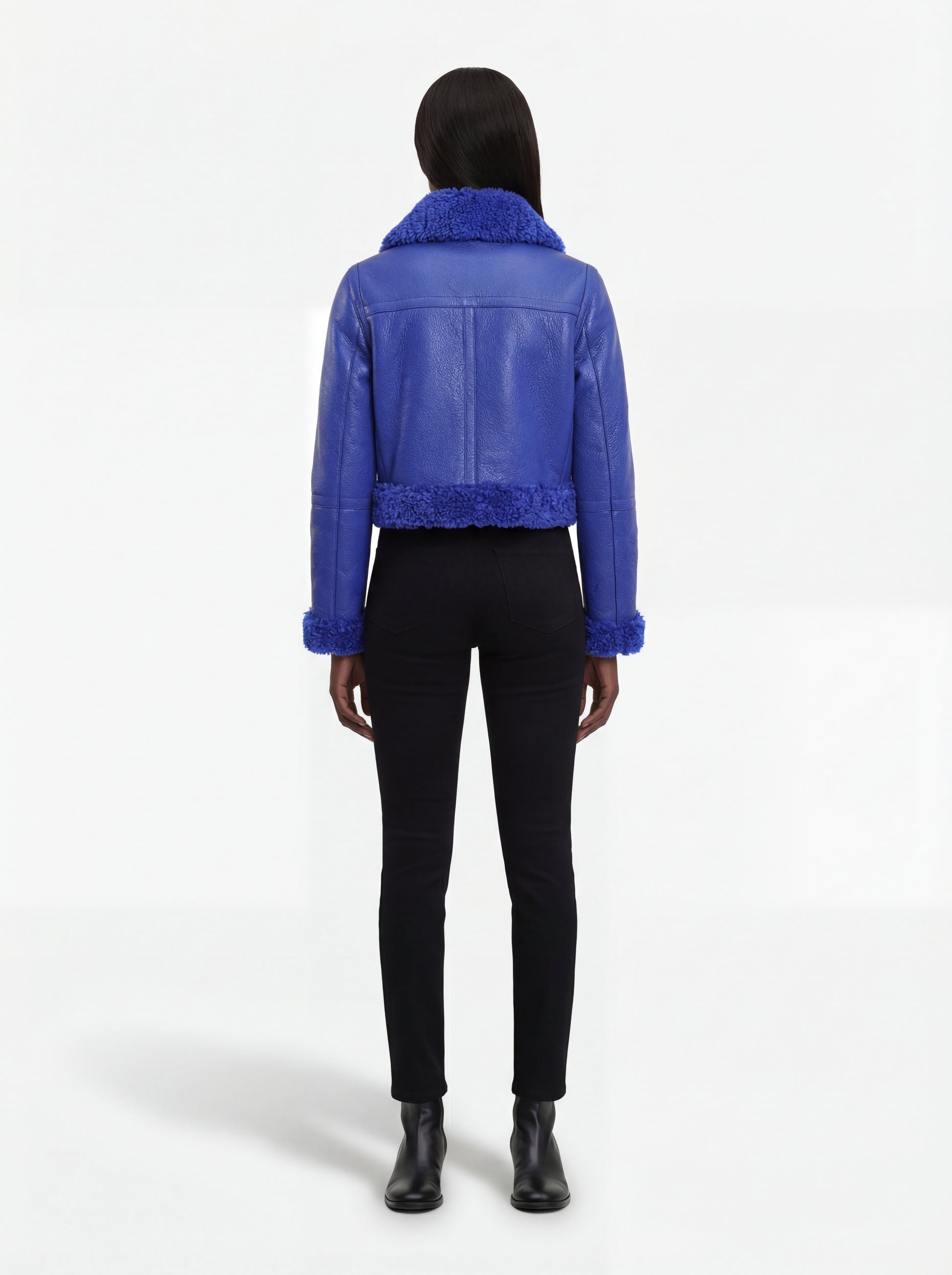 Rear view of female model wearing Maverick Cobalt shearling biker jacket showing structured shoulder fit and blue fur hemline. Maverick Jacket.