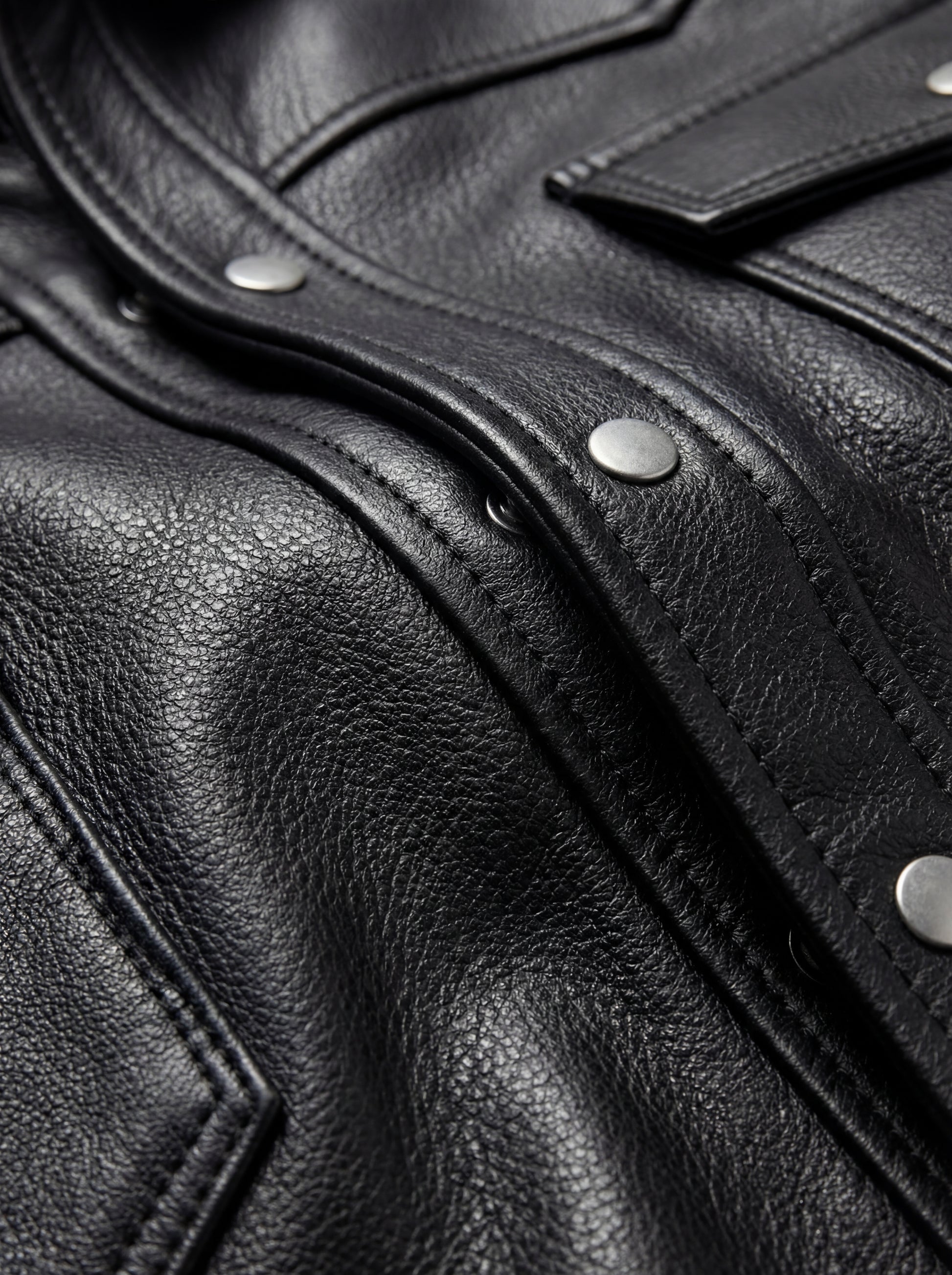 Macro shot of grained black leather texture and silver snap button details on western shirt. Maverick Easton.