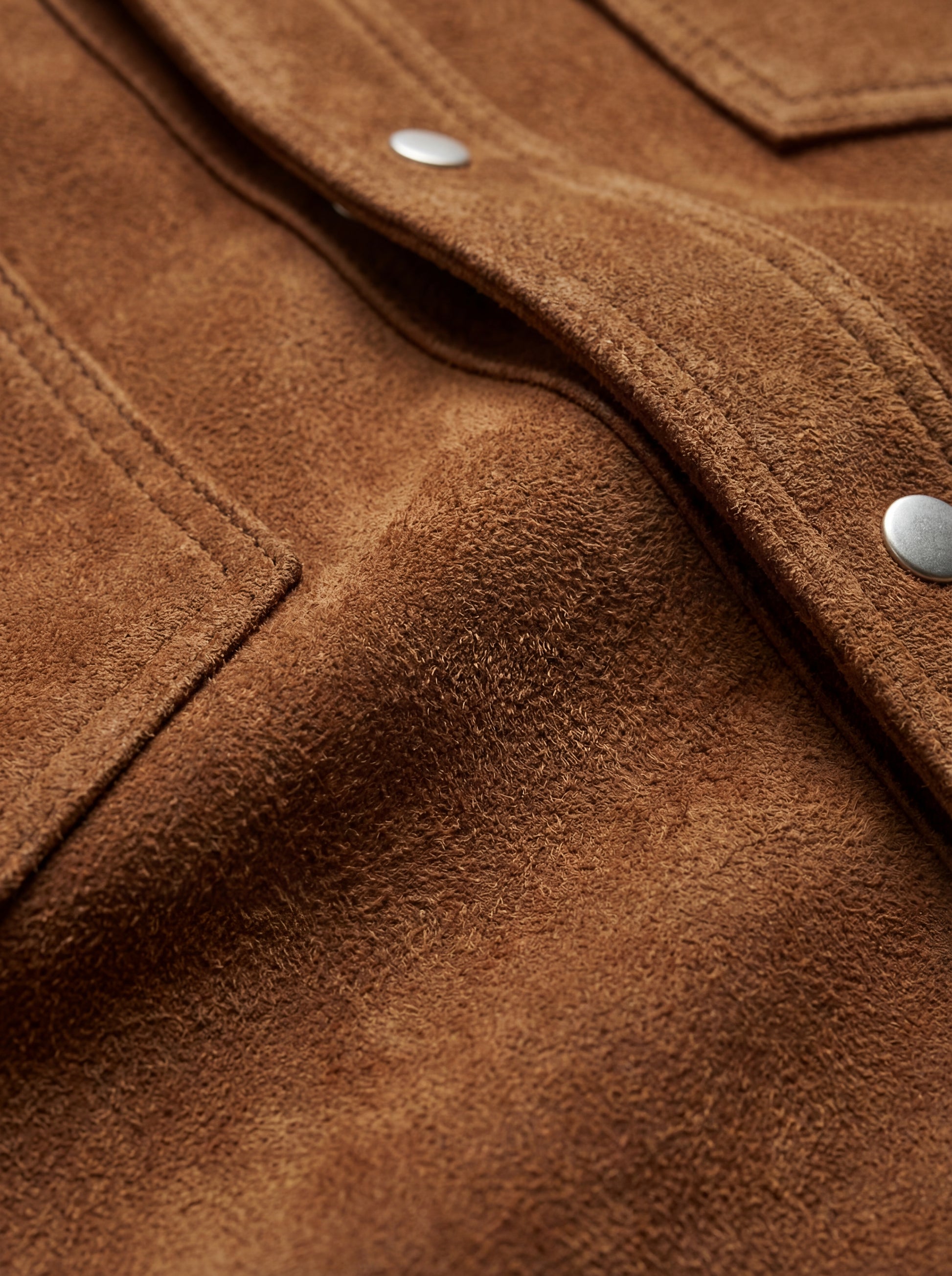 Macro shot of soft tan suede texture and silver snap button detail on western shirt. The Shane by Maverick Jacket.